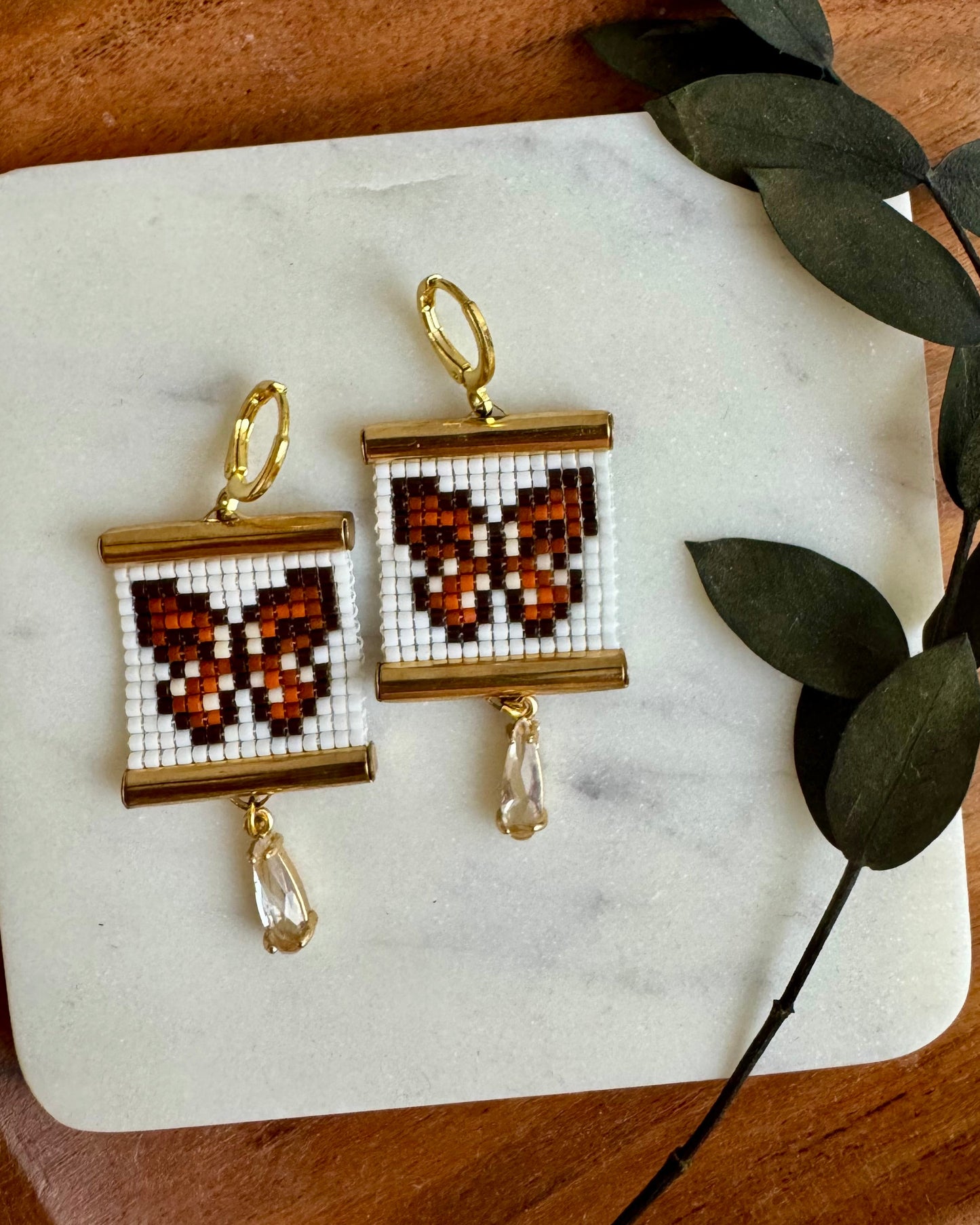 Butterfly-themed earrings on a marble coaster with green leaves