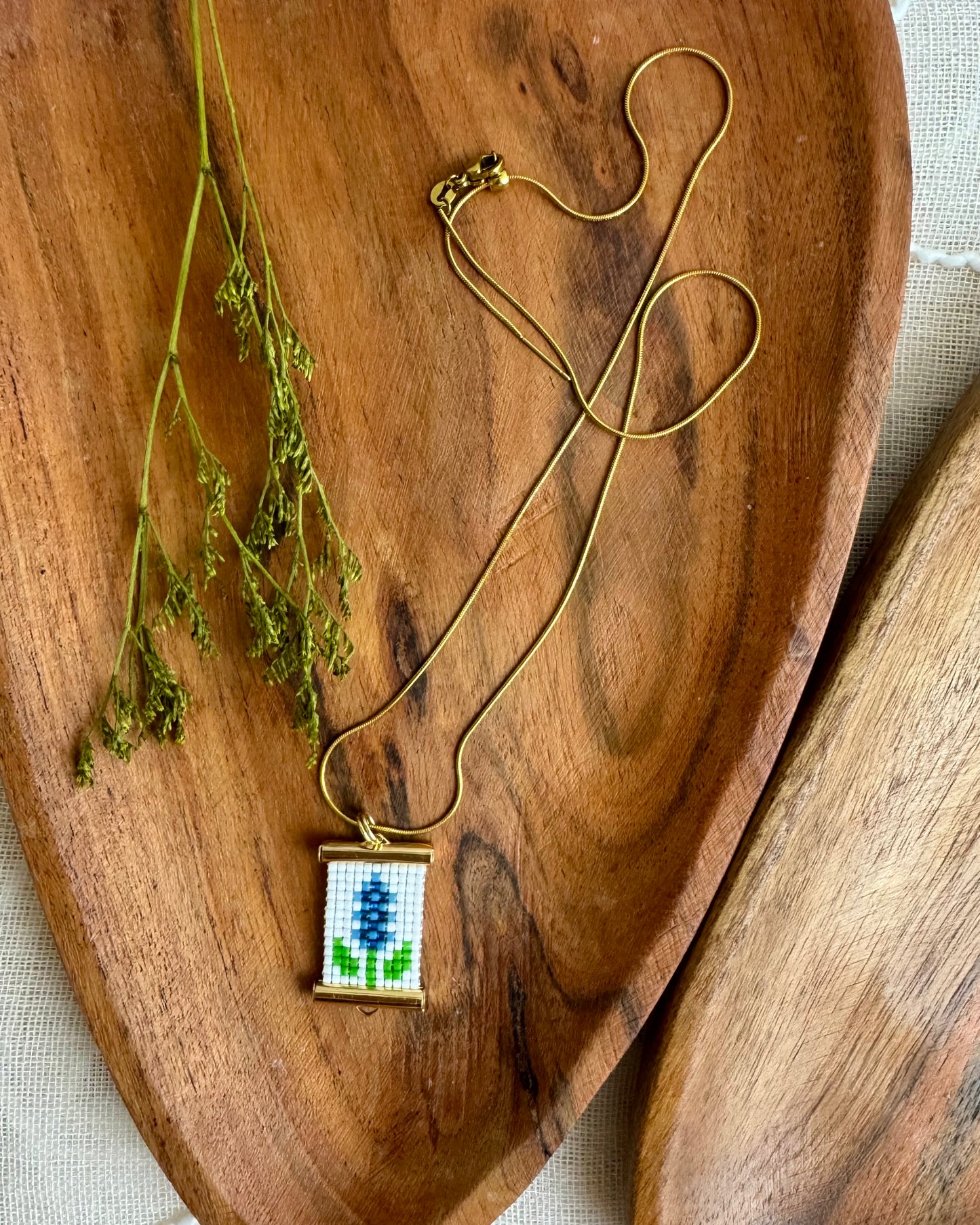 Gold necklace with a small beaded pendant on a wooden surface