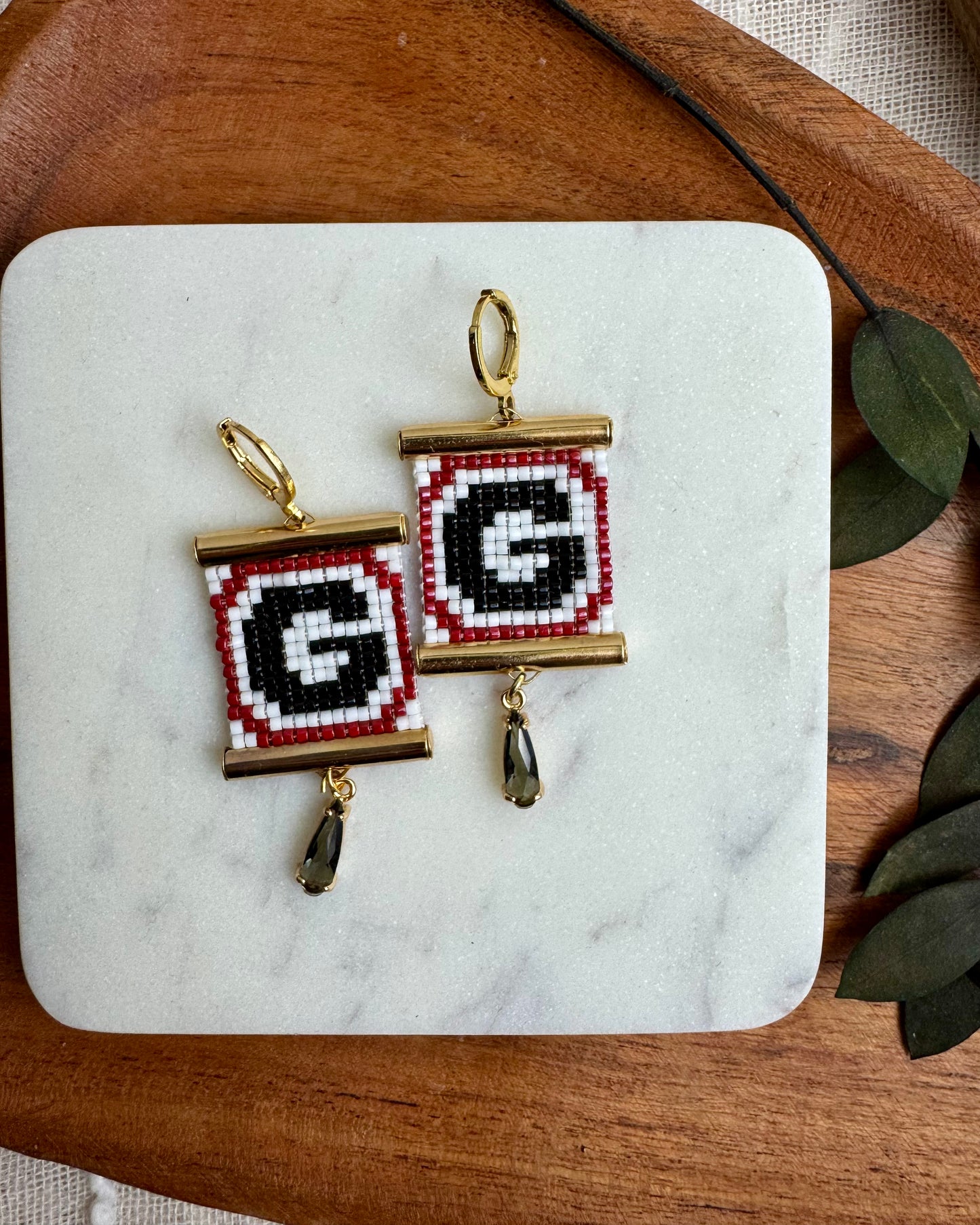 Square pendants with 'G' design on a marble surface