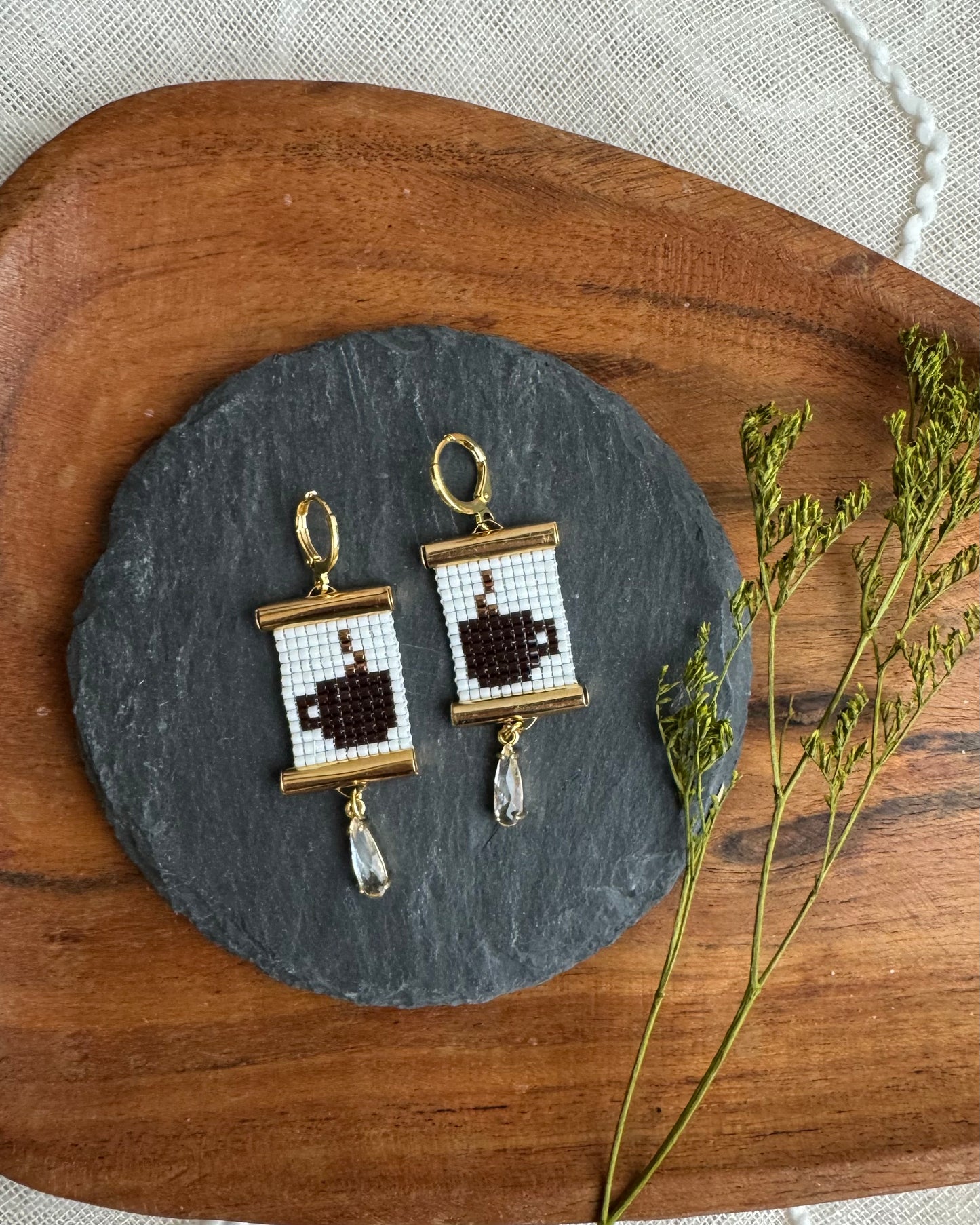 Pair of earrings with coffee cup design on a slate stone with wooden and fabric background