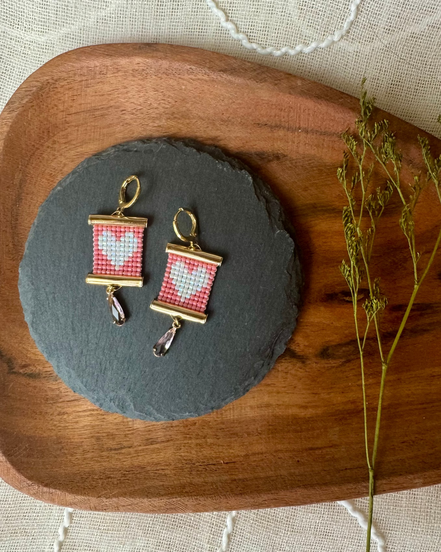 Earrings with heart design on a slate stone, placed on a wooden tray with a natural background.