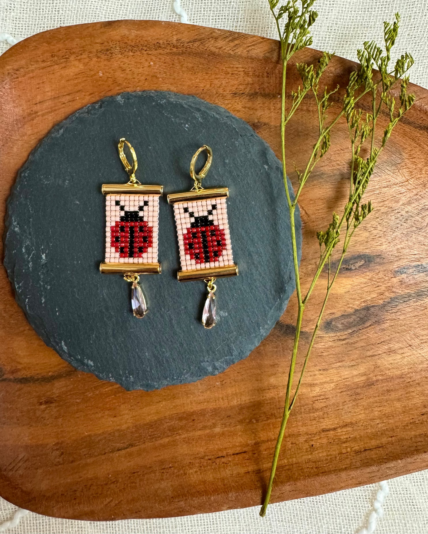 Beaded earrings with gold hardware depicting ladybugs on a slate platter.