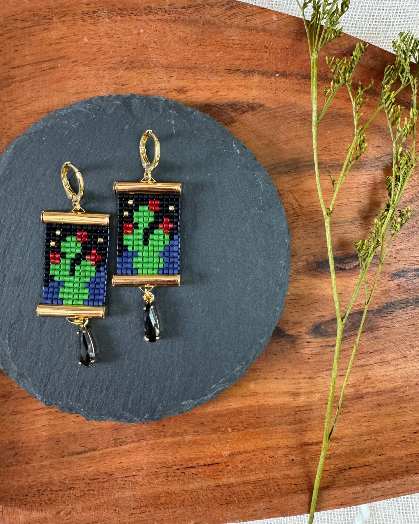 Beaded earrings with gold hardware depicting prickly pear cactii on a slate platter.