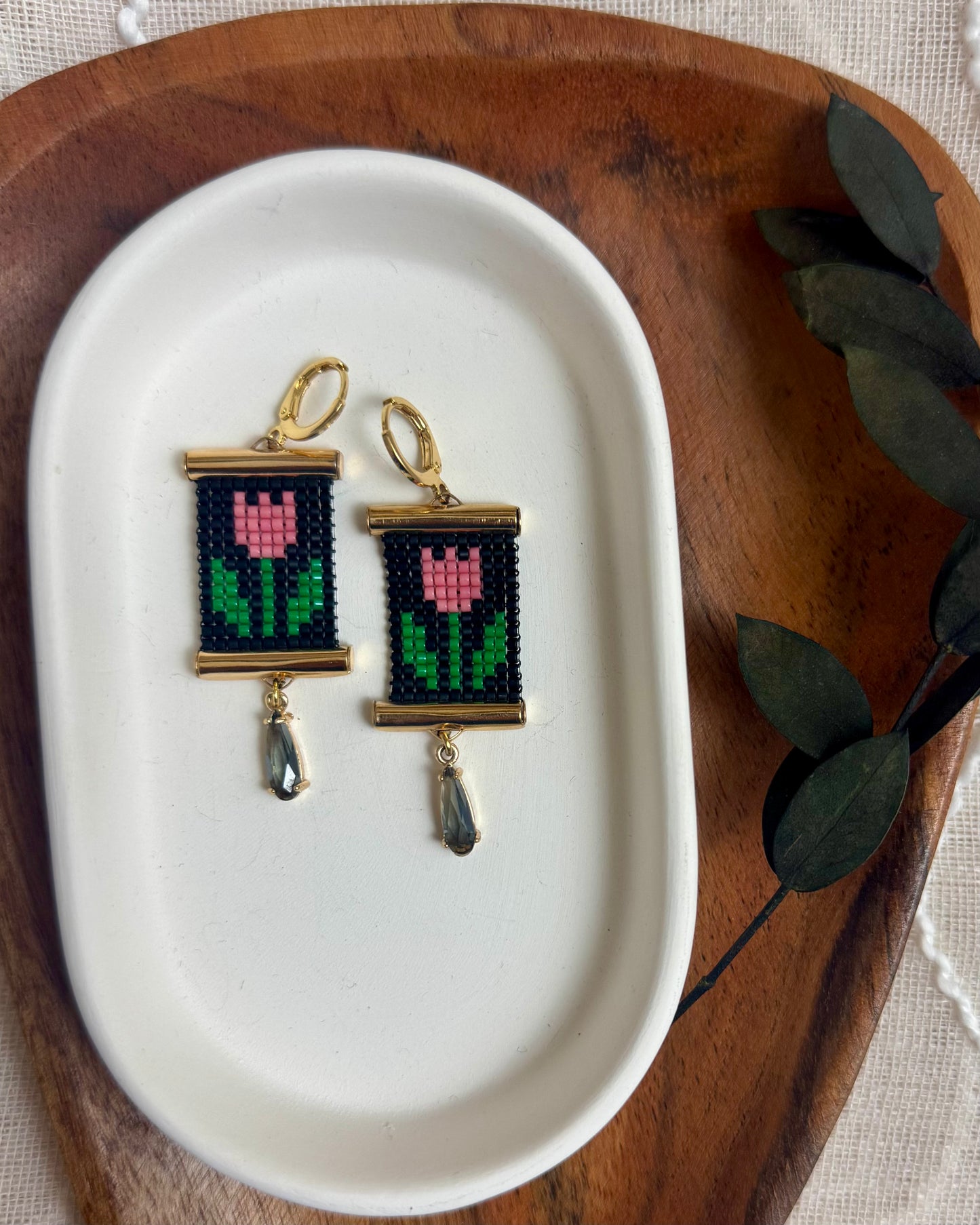 Pair of earrings with beaded tulip design on a white dish with a wooden border.