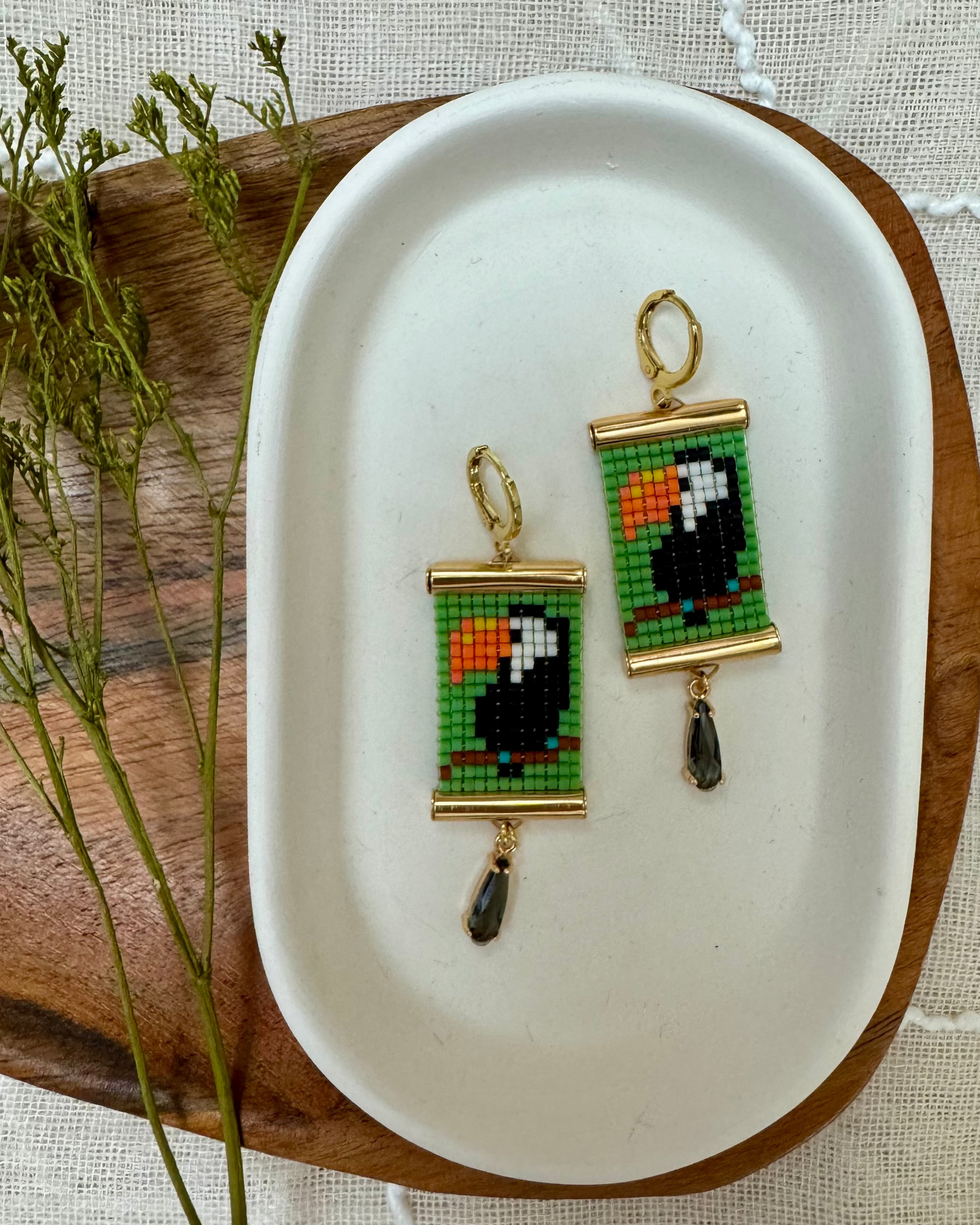 Pixelated toucan earrings on a white dish with a wooden edge.