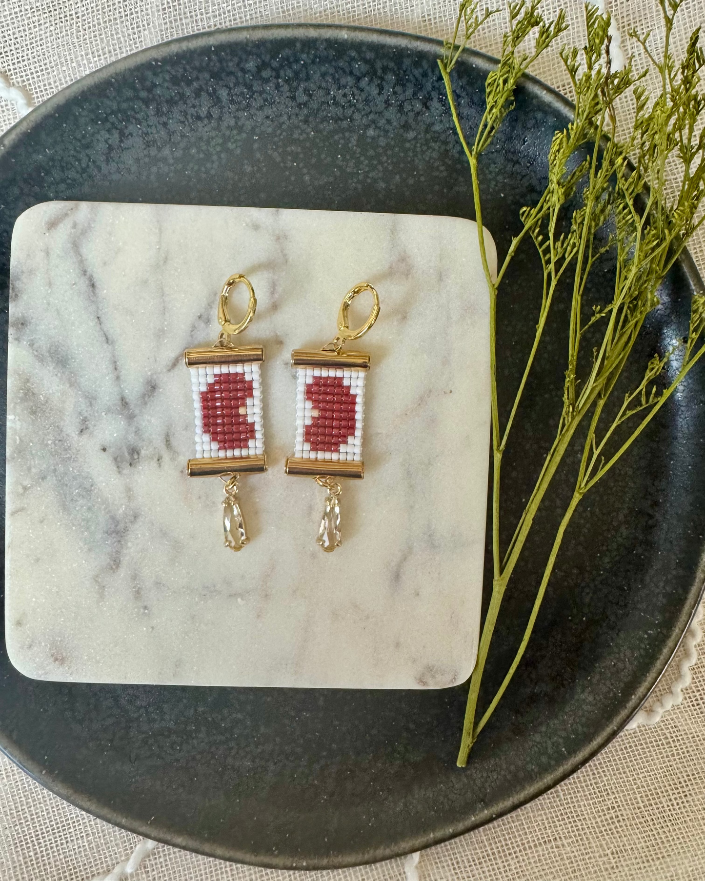 Pair of beaded earrings depicting kidney beans on a marble coaster with a decorative branch on a textured surface
