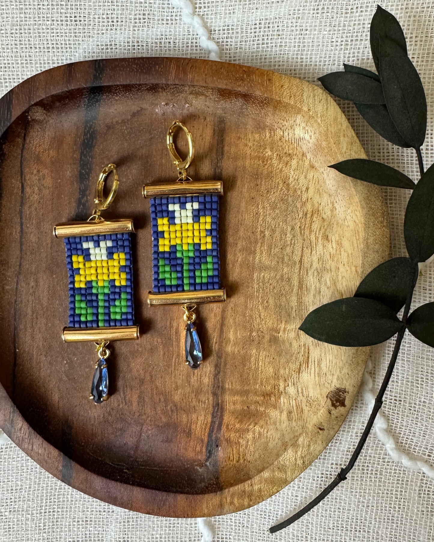 Pair of earrings with colorful daffodil design on a wooden tray