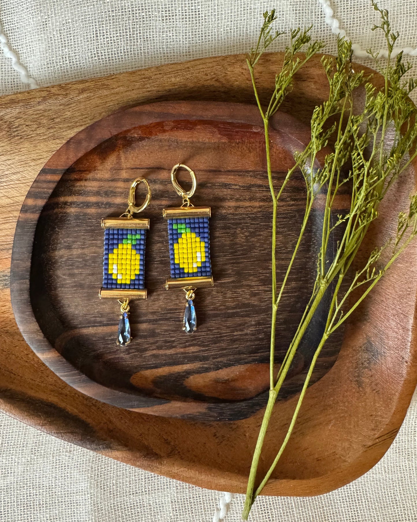 Pair of beaded earrings with lemon design on a wooden tray with dried plants
