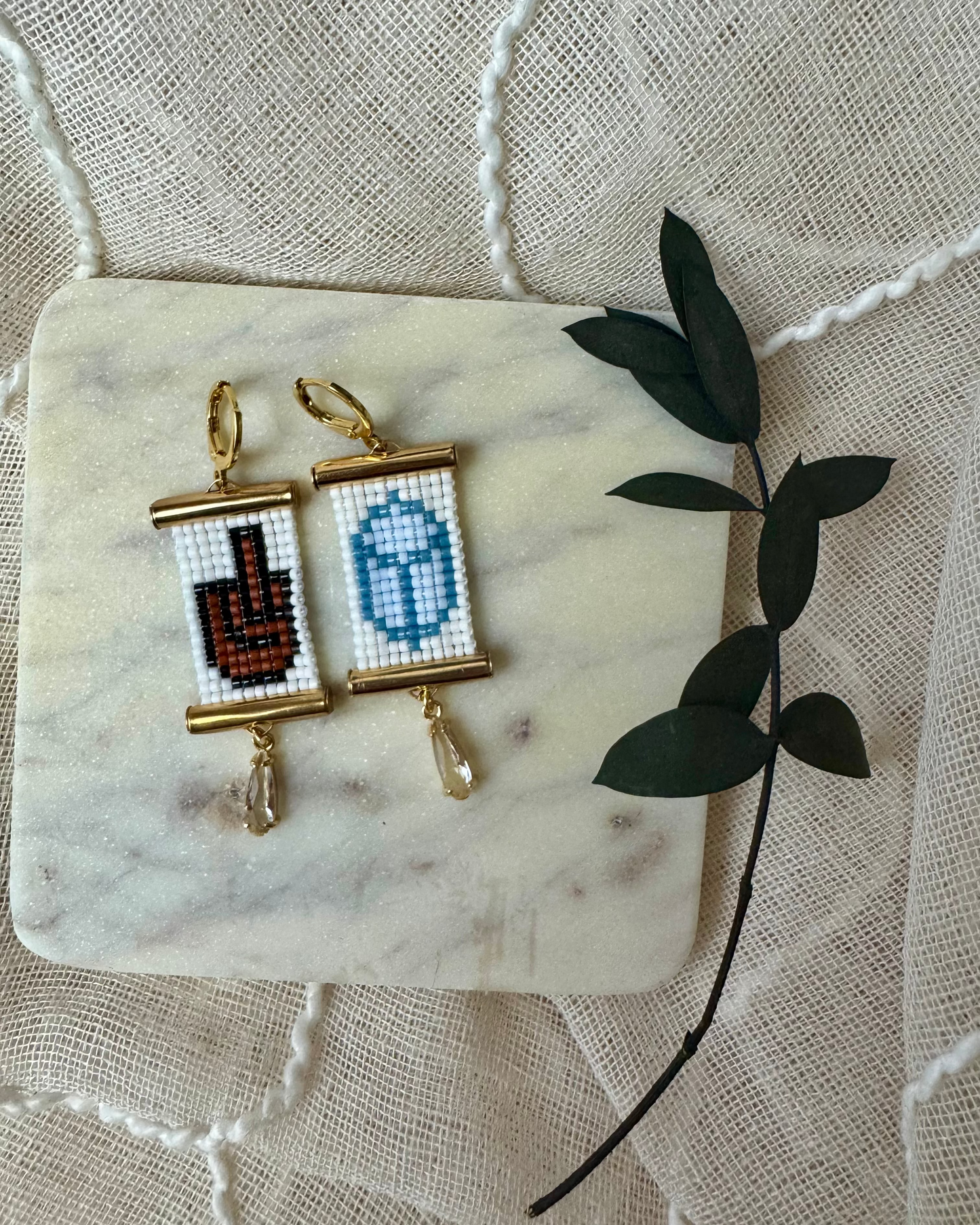 Pair of beaded earrings on a marble surface with a decorative leaf