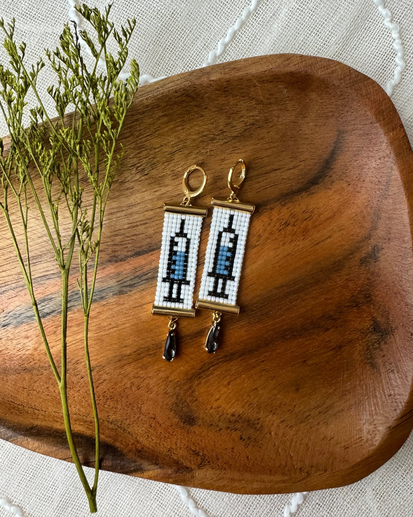 Pair of earrings on a wooden surface with a white lace background