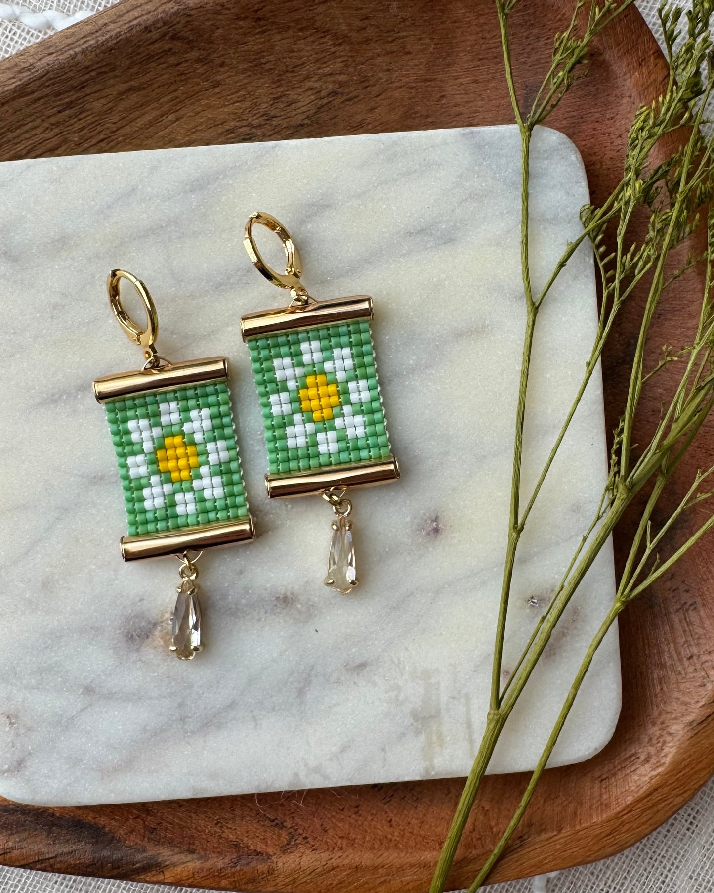 Beaded earrings with daisy pattern on a marble surface with a wooden tray.