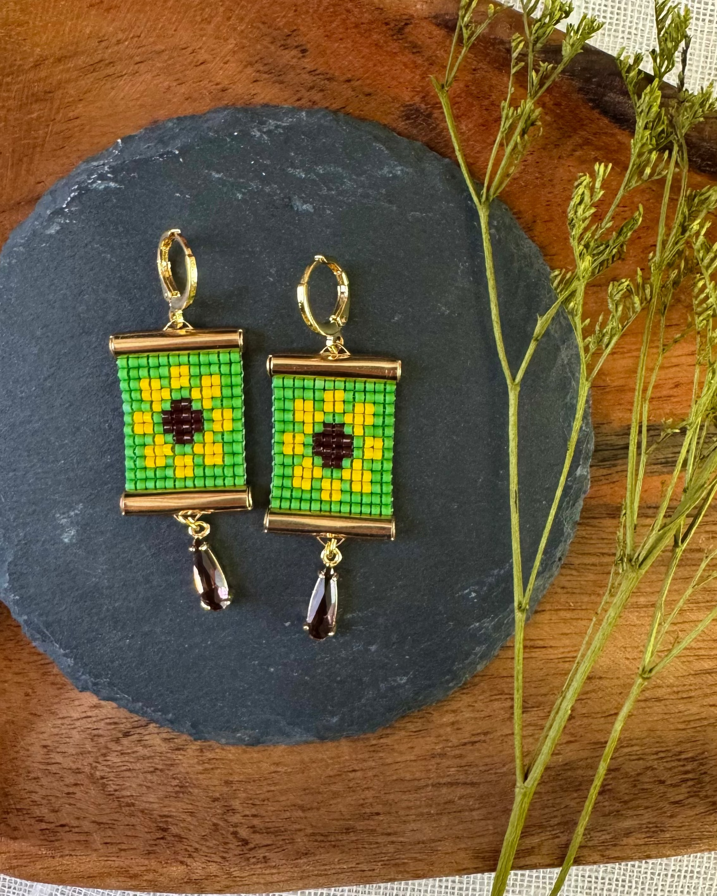 Beaded earrings on a dark slate surface with a wooden and fabric background