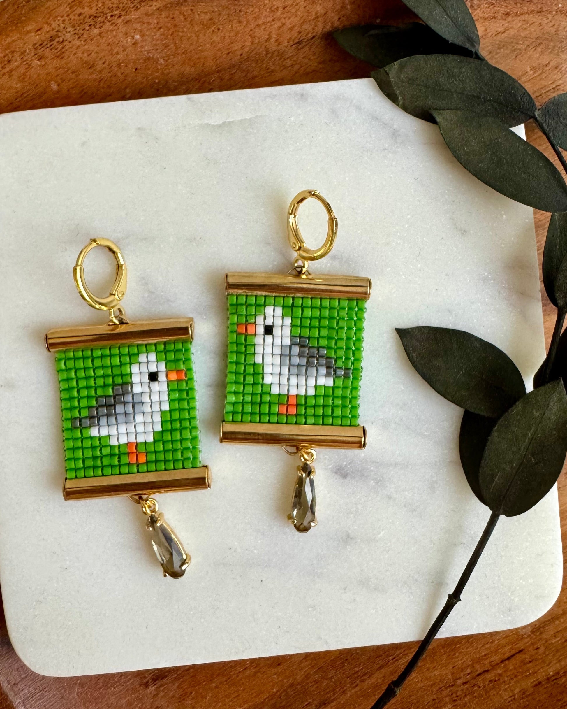 Pair of earrings with bird design on a marble stone with leaves