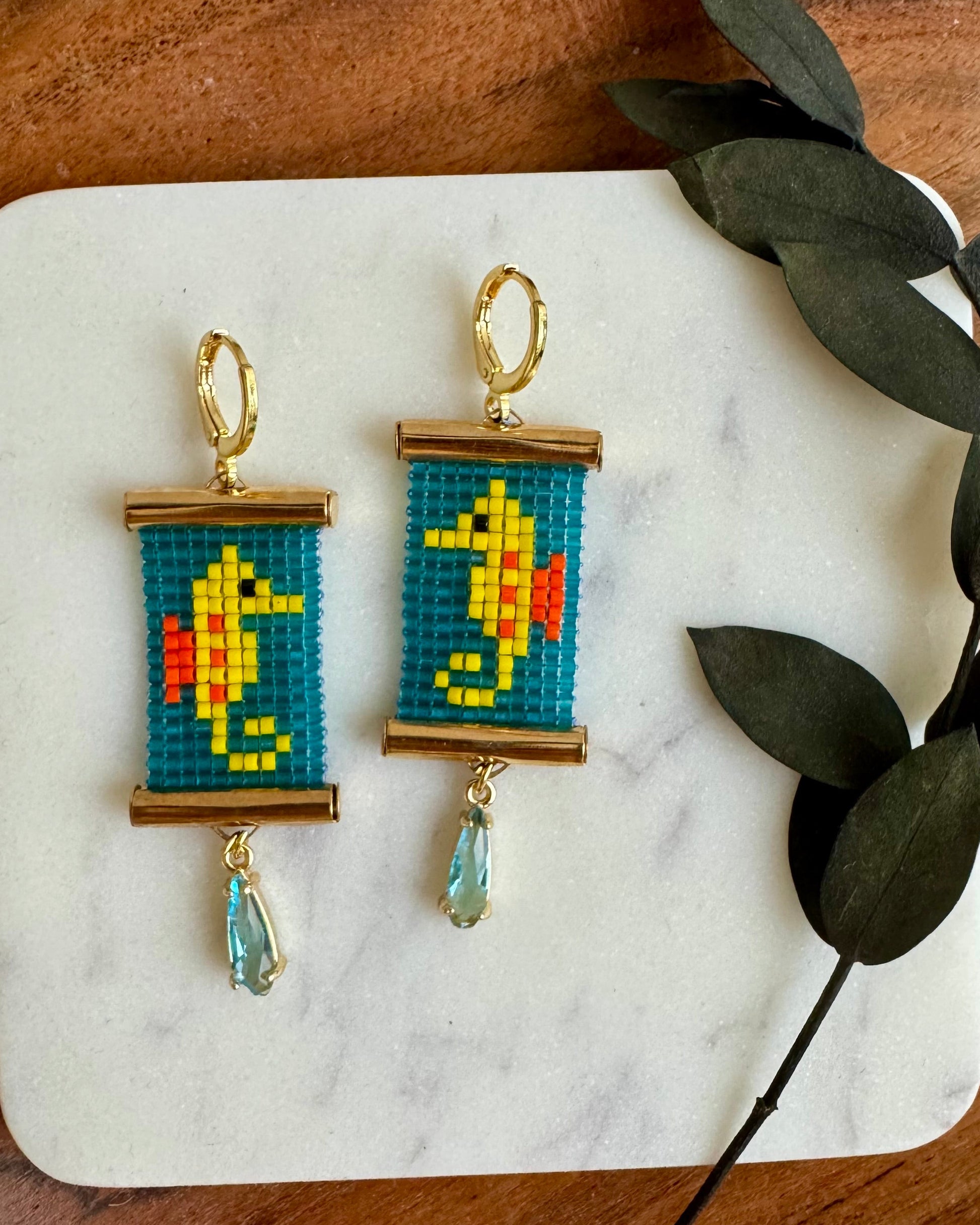 Pair of earrings with beadwork on a marble coaster with leaves.