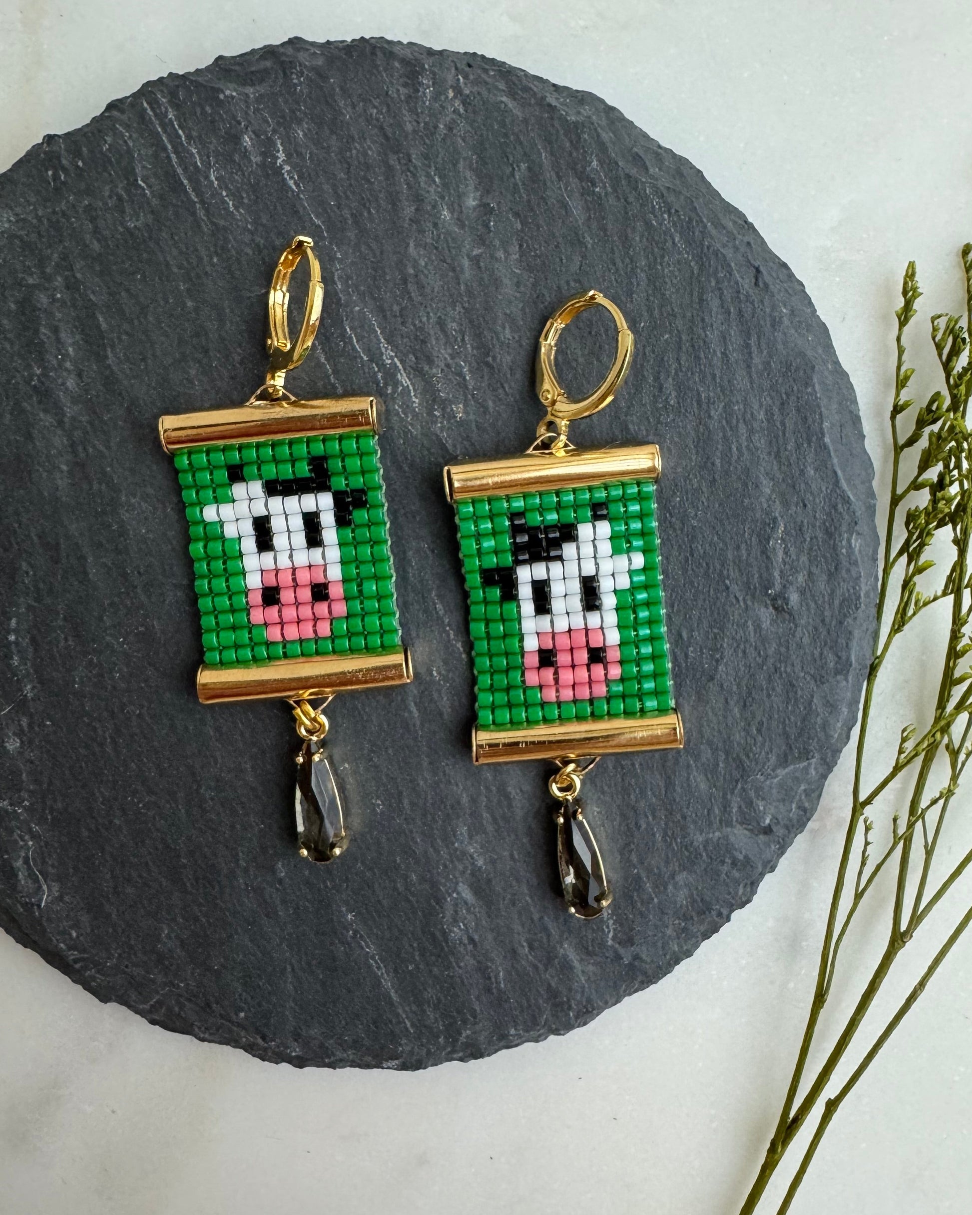 Pixelated cow earrings on a round slate stone with a white background