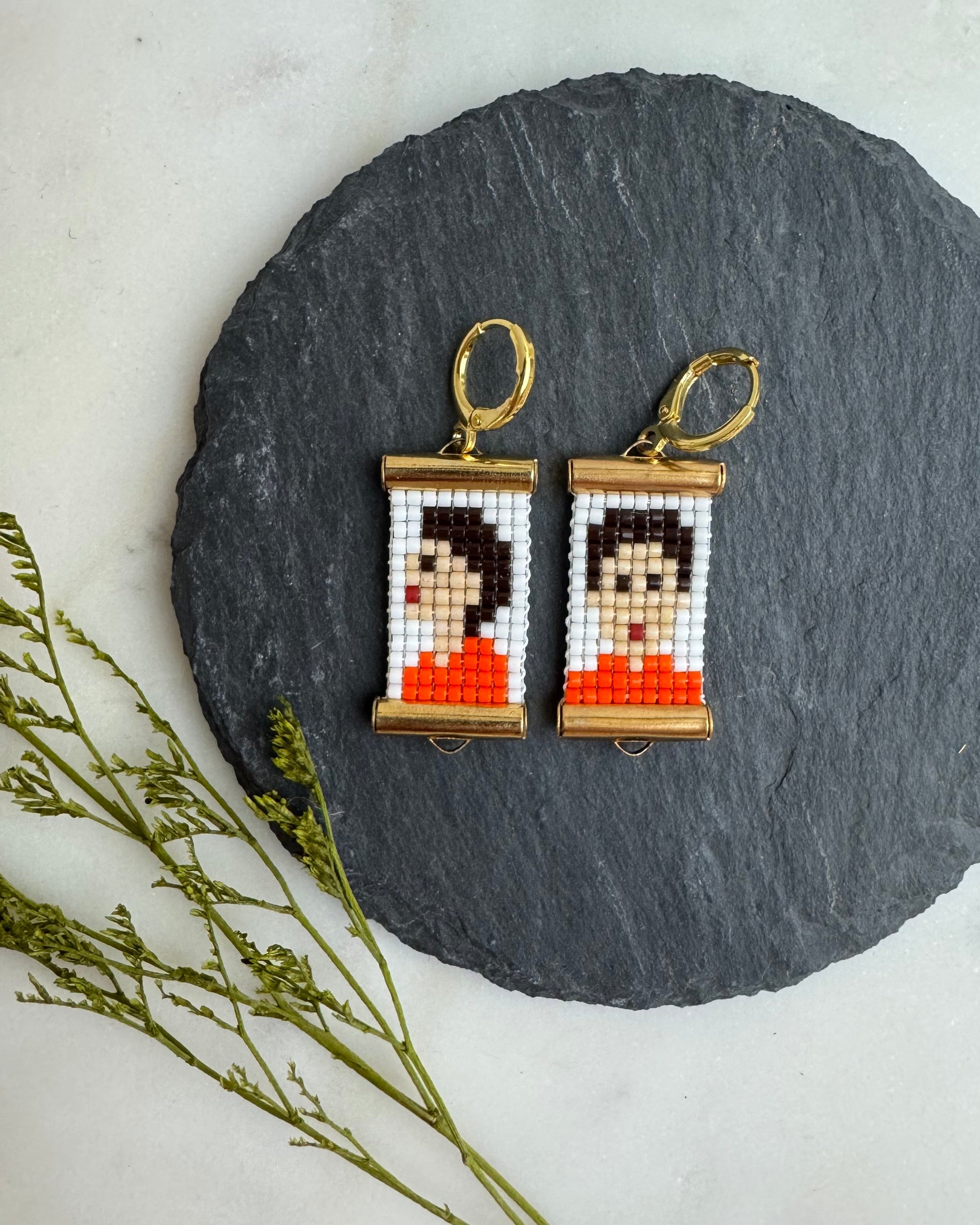Pixelated earrings on a round black stone surface with a white background