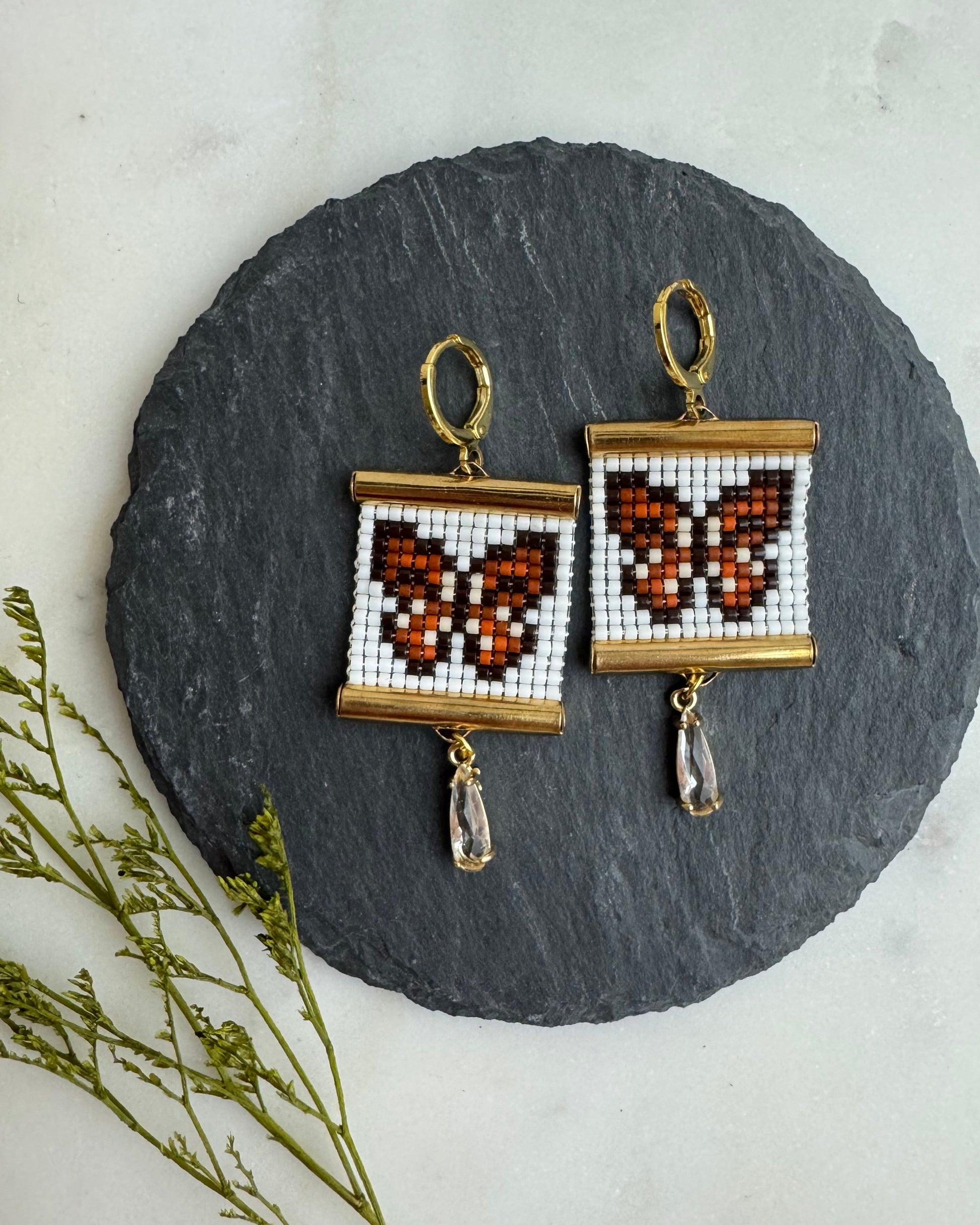 Butterfly-themed beaded earrings on a round slate stone with a light background