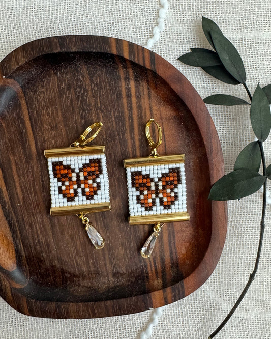 Pair of butterfly earrings on a wooden tray with a natural background