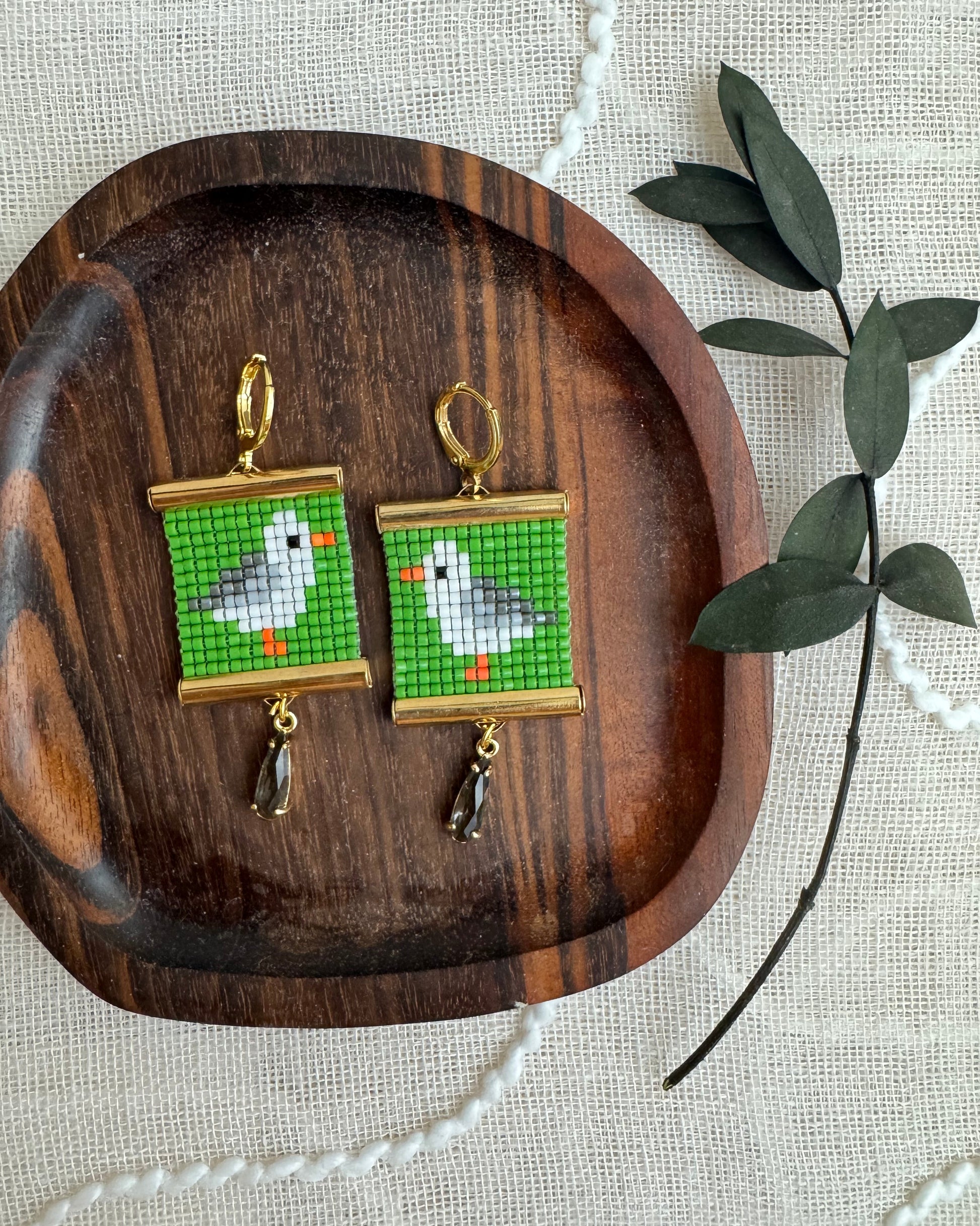 Pair of earrings with bird design on a wooden tray