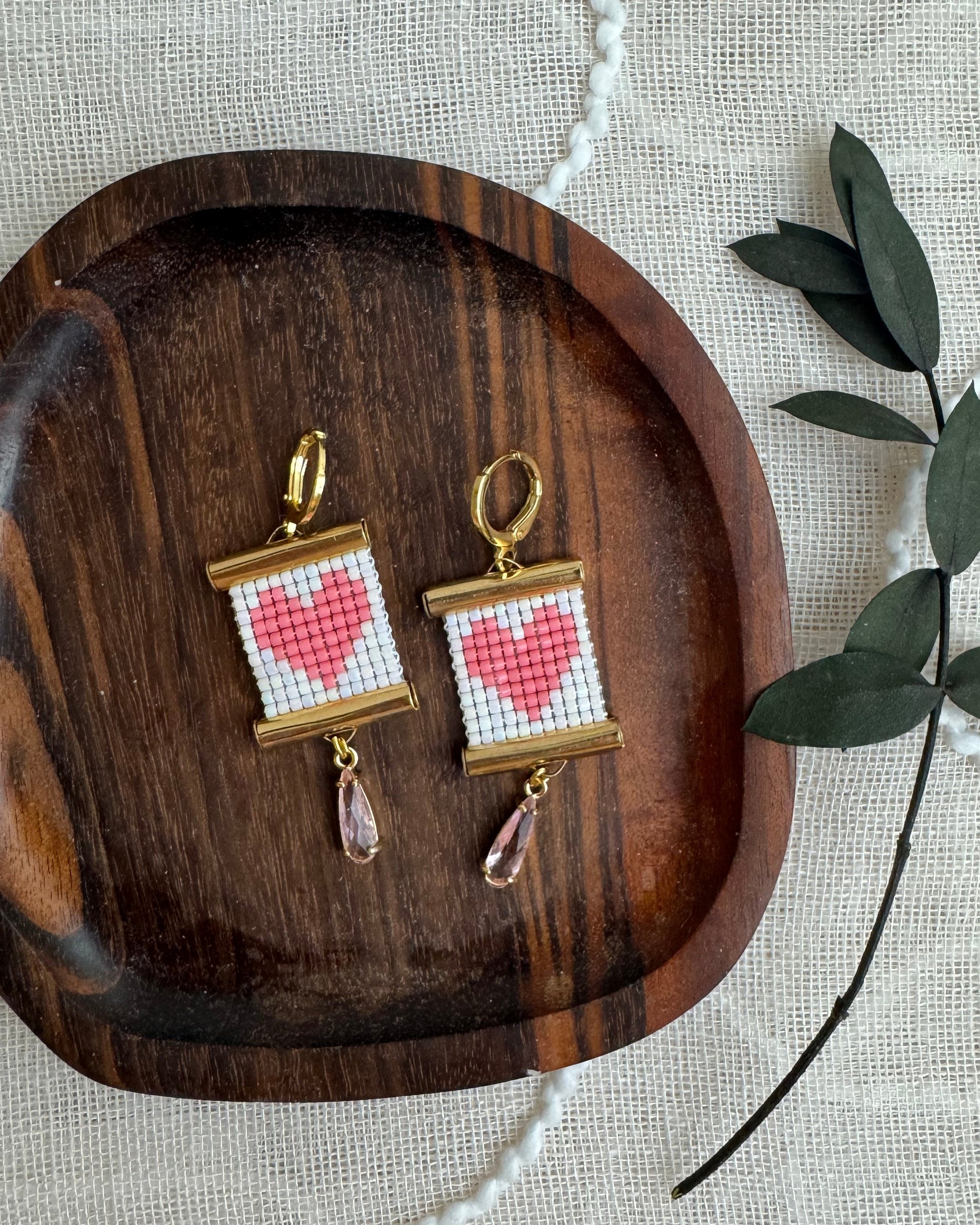 Pair of earrings with heart design on a wooden tray with a light background