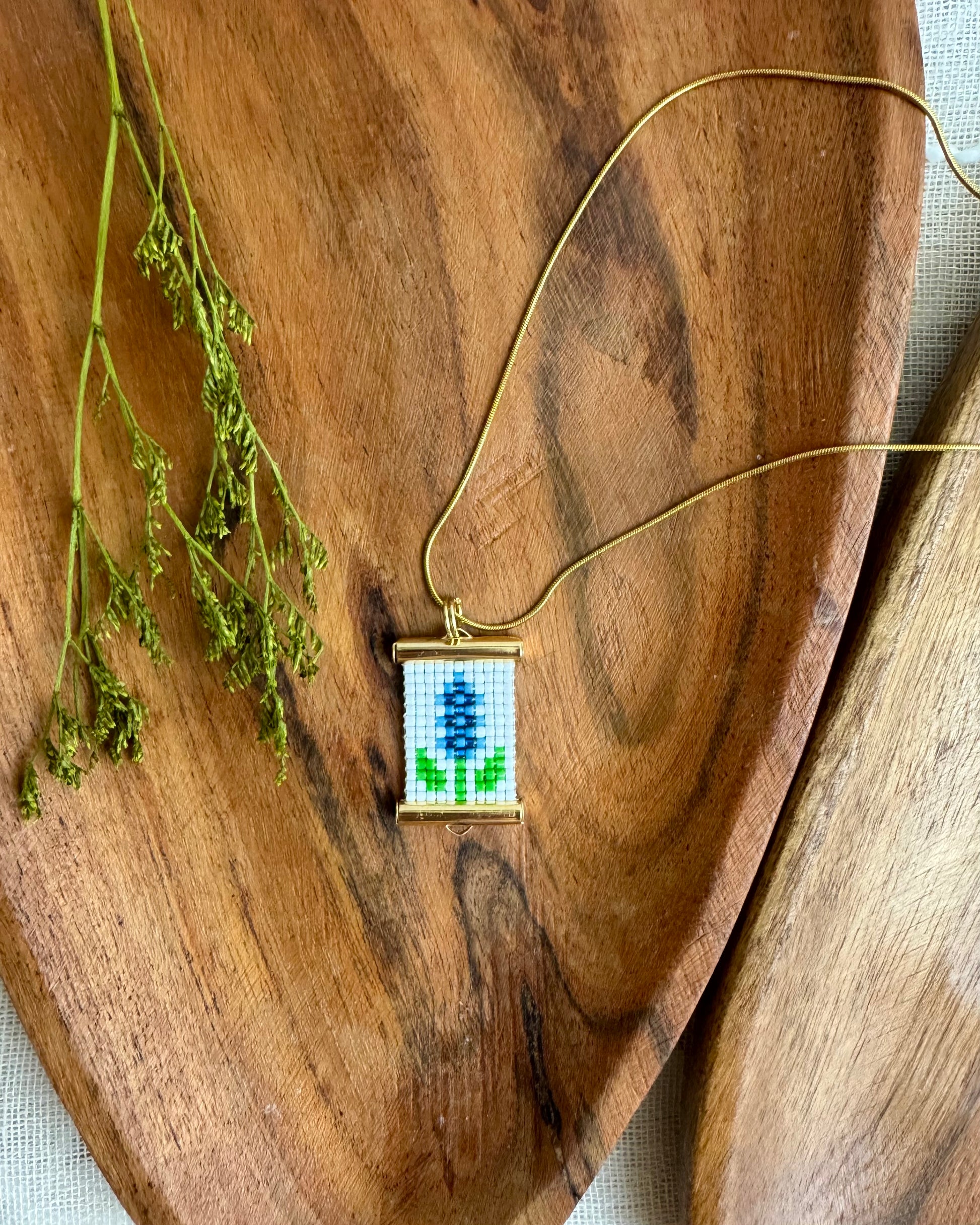 Necklace with a pendant featuring a blue flower design on a wooden surface.