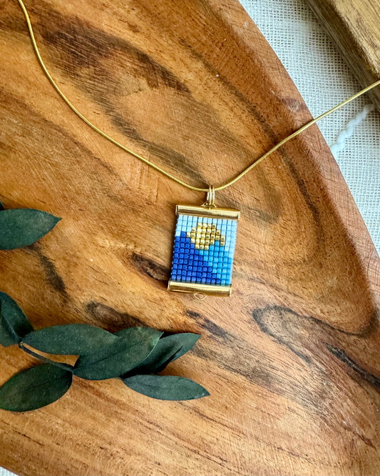 Necklace with a mountain pendant on a wooden surface with leaves