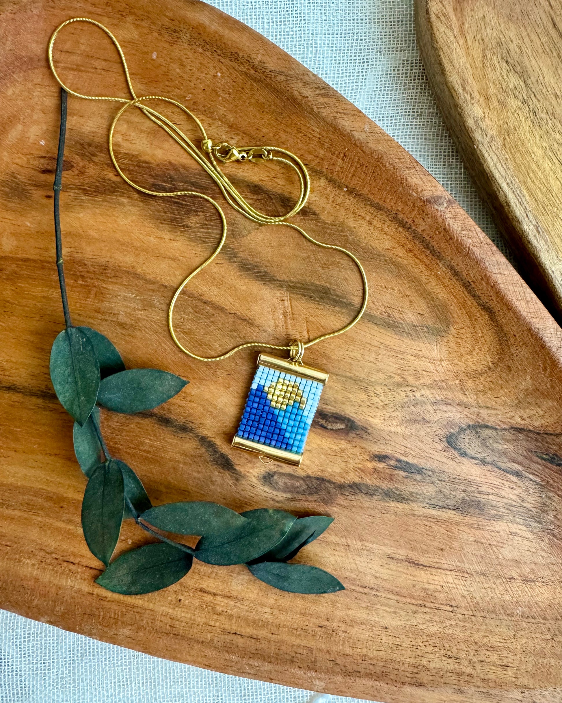 Gold necklace with a blue and gold pendant on a wooden surface