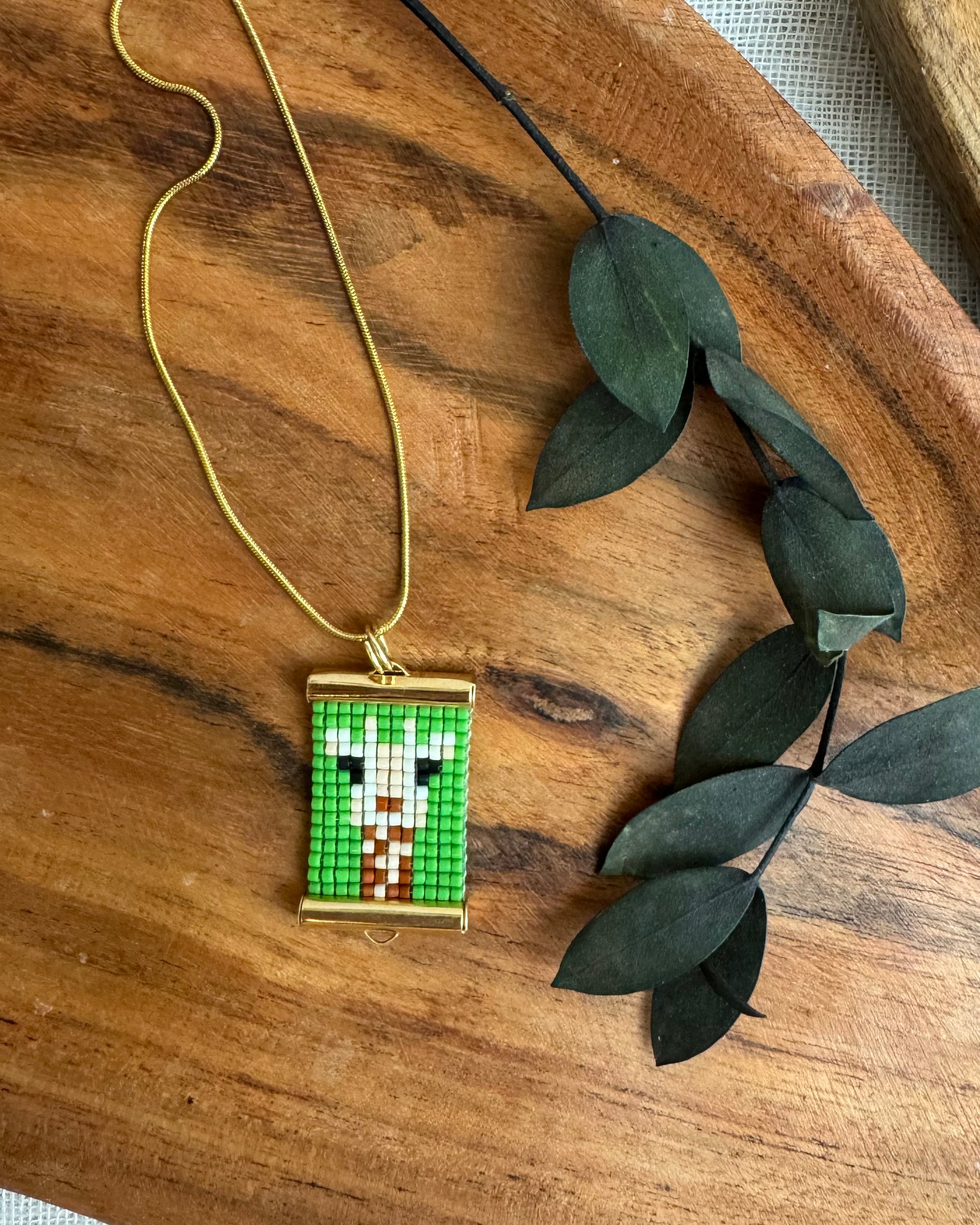 Pixelated pendant necklace on a wooden surface with green leaves