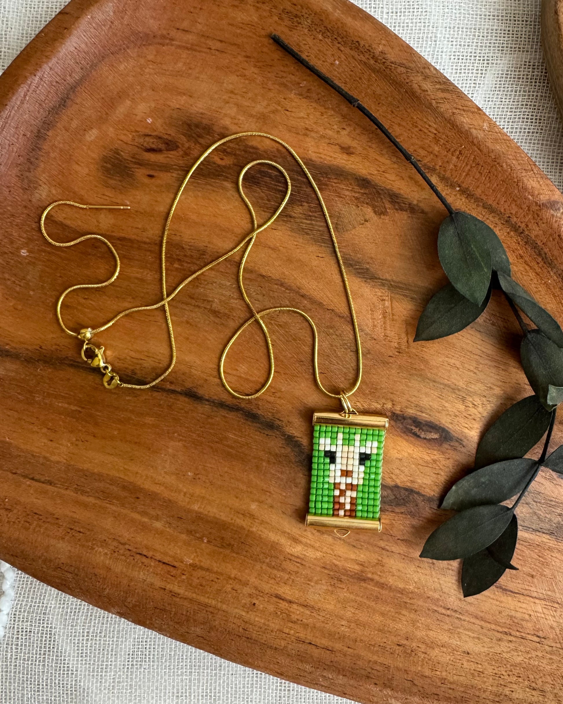 Gold necklace with a pixelated giraffe pendant on a wooden surface with leaves.