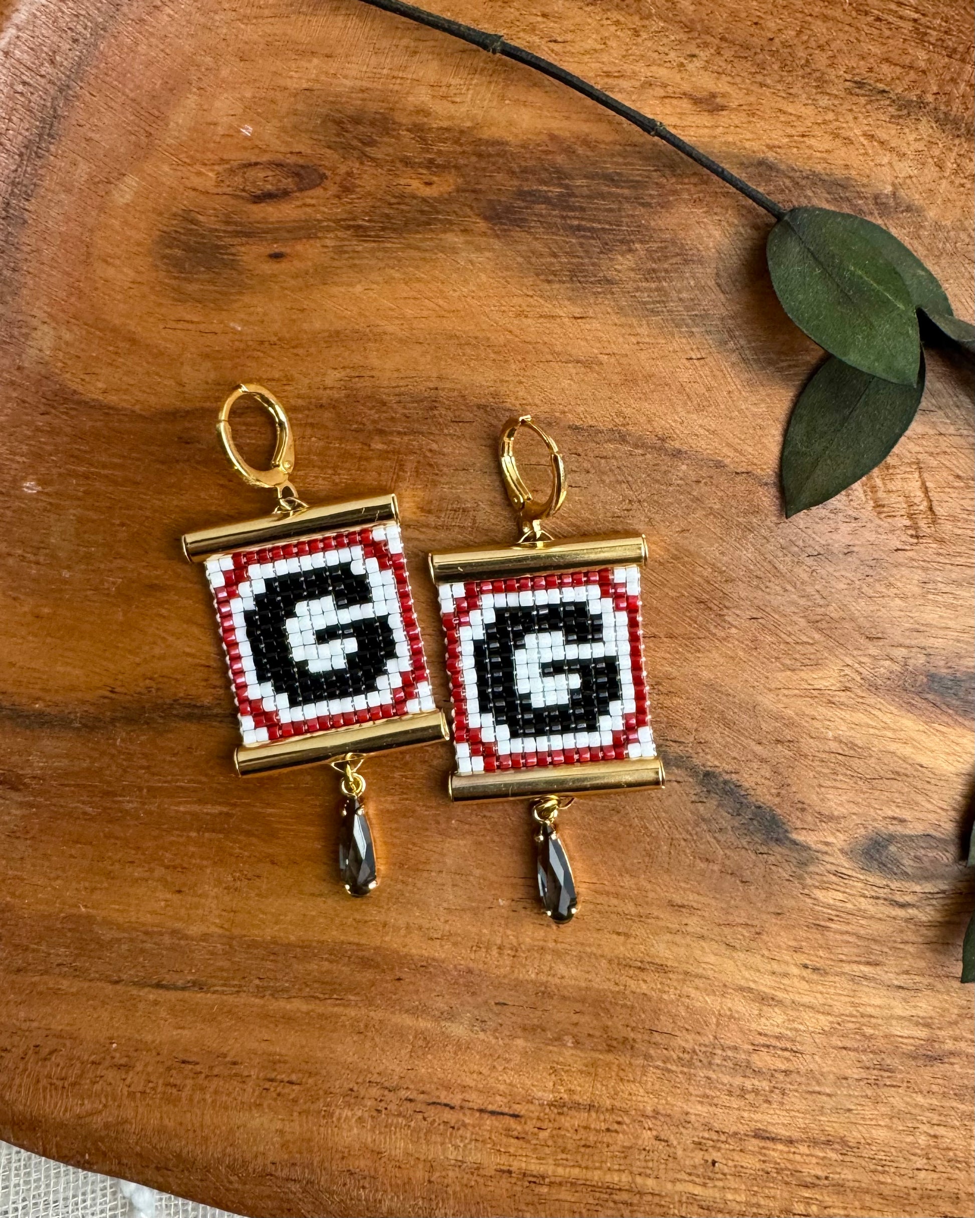 Pair of earrings with 'G' design on a wooden surface