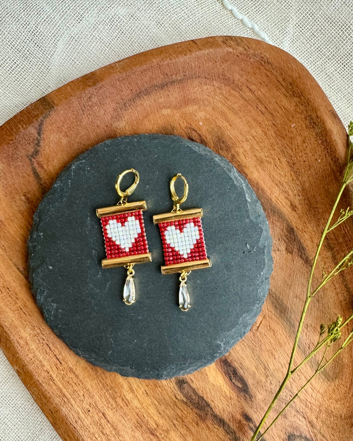 Pair of earrings with heart design on a dark slate stone, placed on a wooden surface.