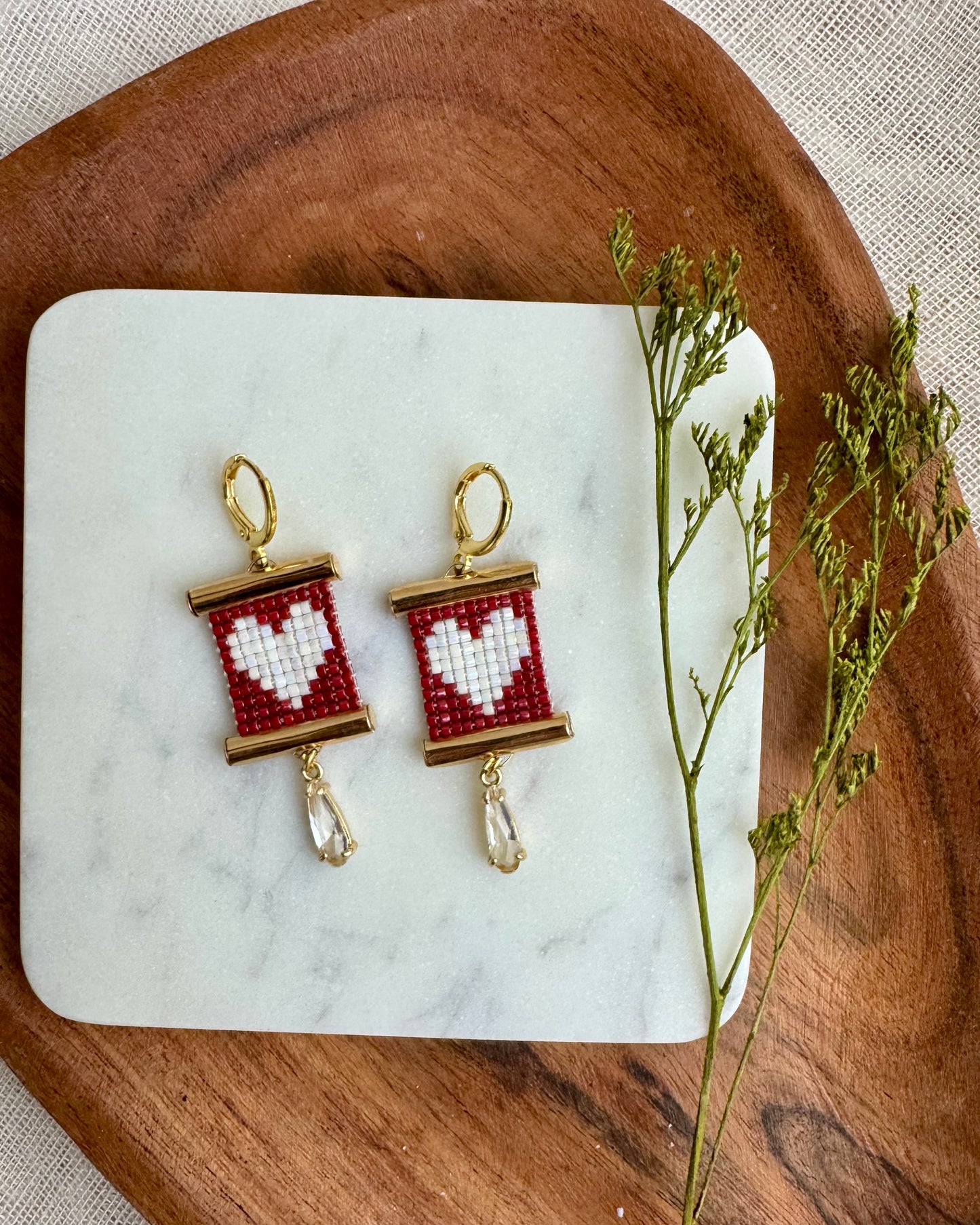 Pair of earrings with heart design on a marble coaster with a wooden surface and plant.
