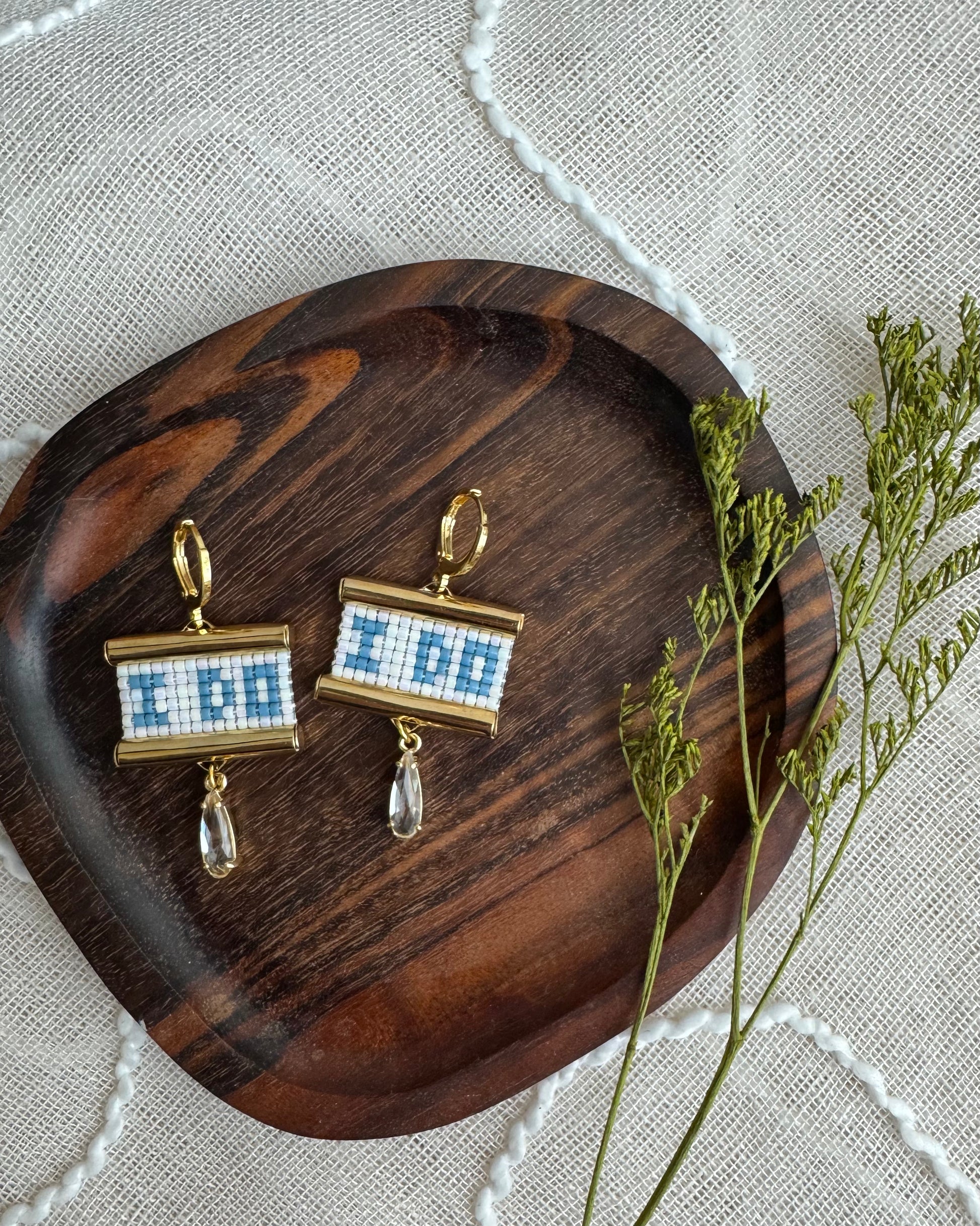 Pair of earrings with 'I DO' text on a wooden tray with a textured fabric background