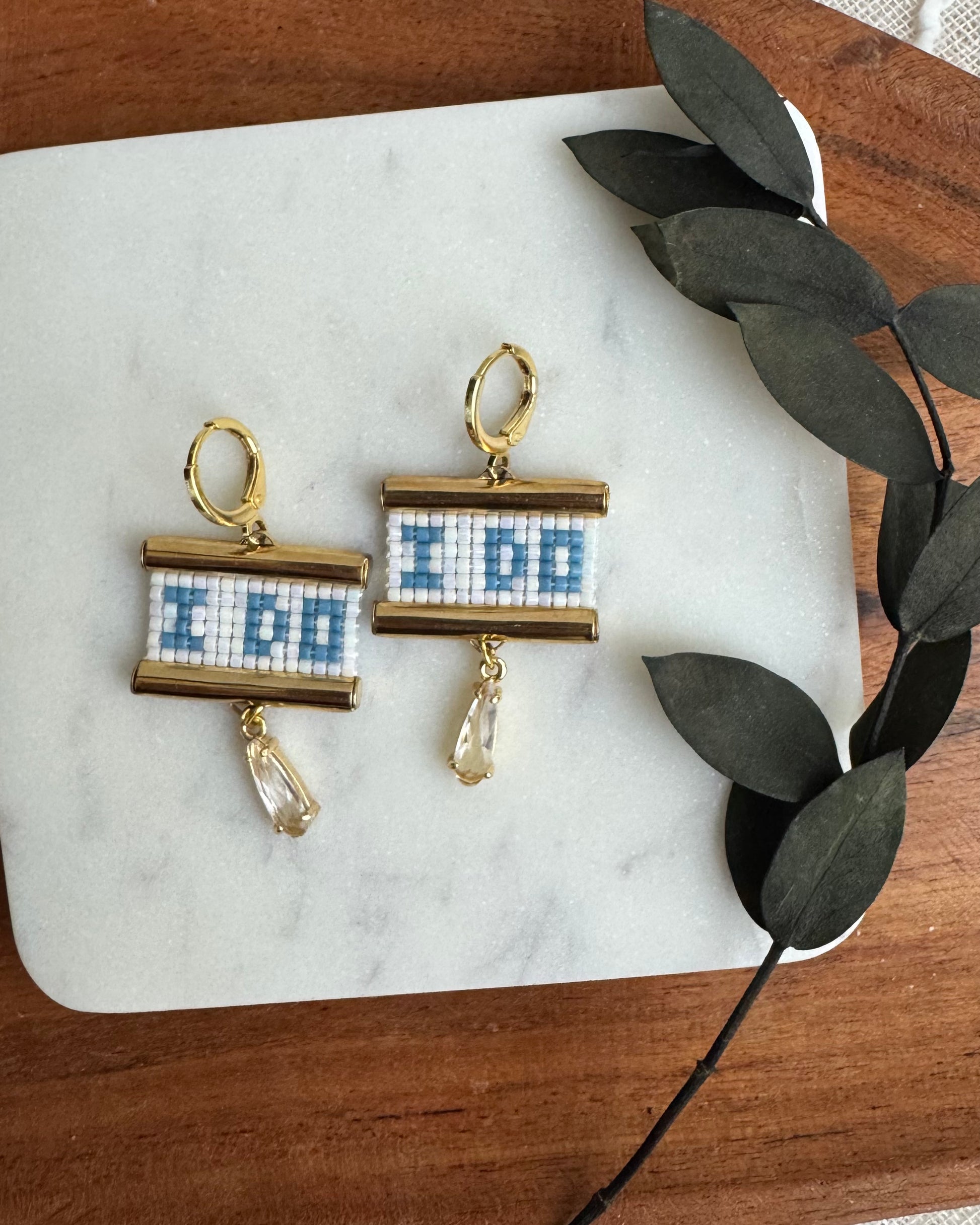 Pair of earrings with blue and white design on a marble surface with leaves.