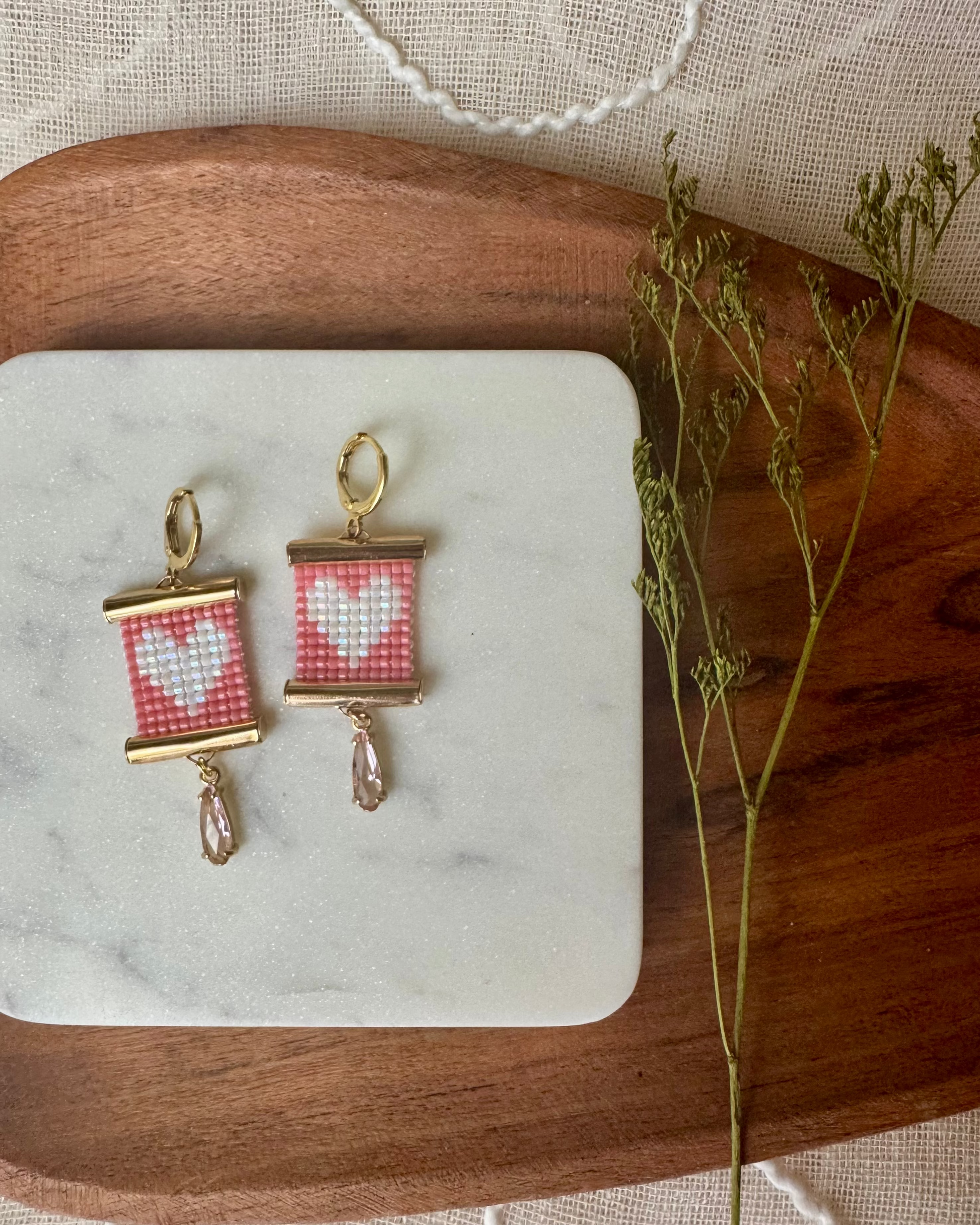 Pair of earrings with pink and white pattern on a marble stone with wooden and fabric background