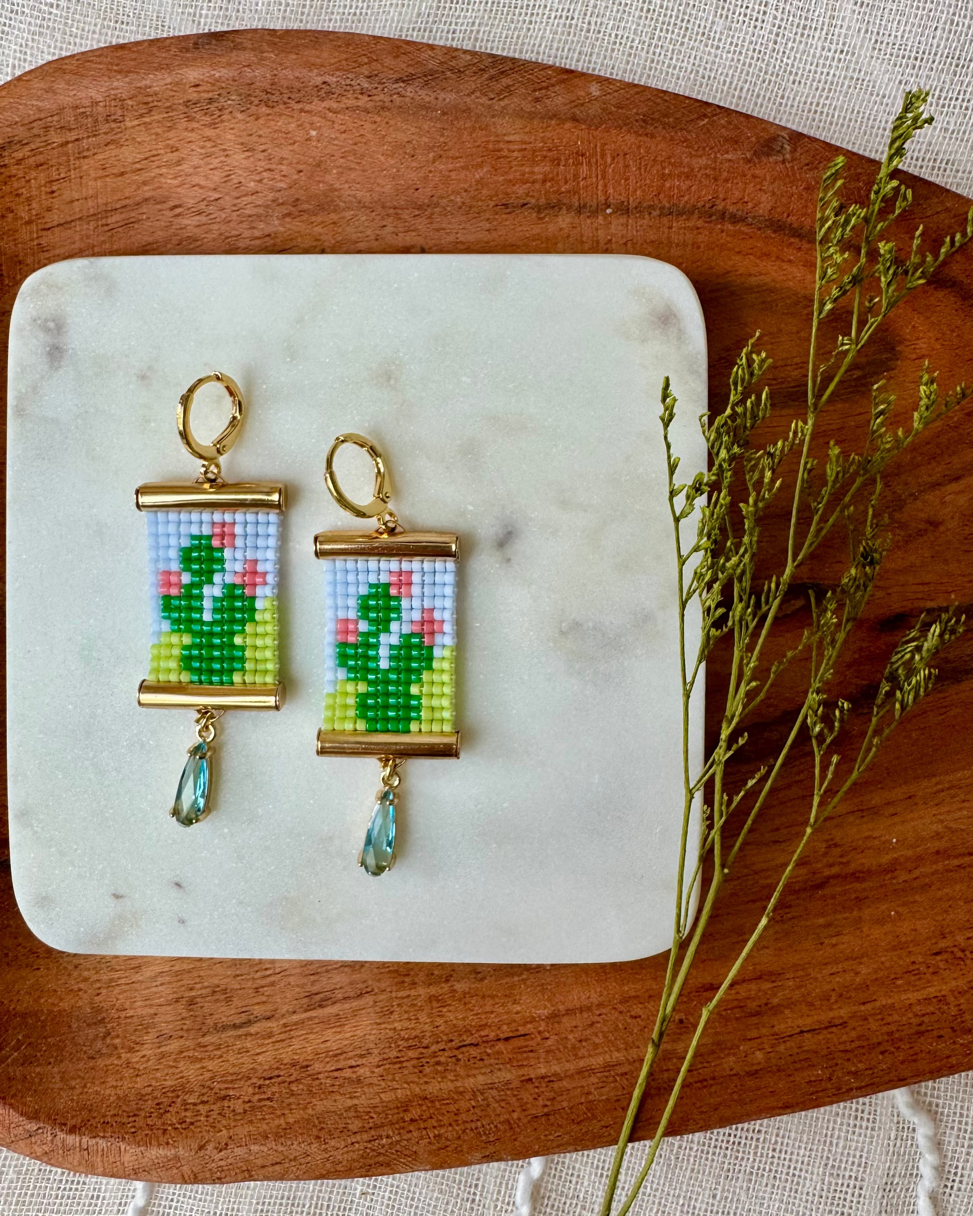 Pair of earrings with beaded prickly pear cactus design on a marble coaster with a wooden edge.