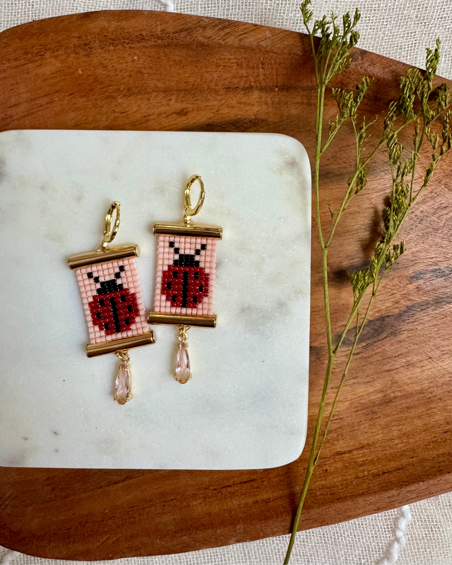 Beaded earrings with gold hardware depicting ladybugs on a wooden platter.