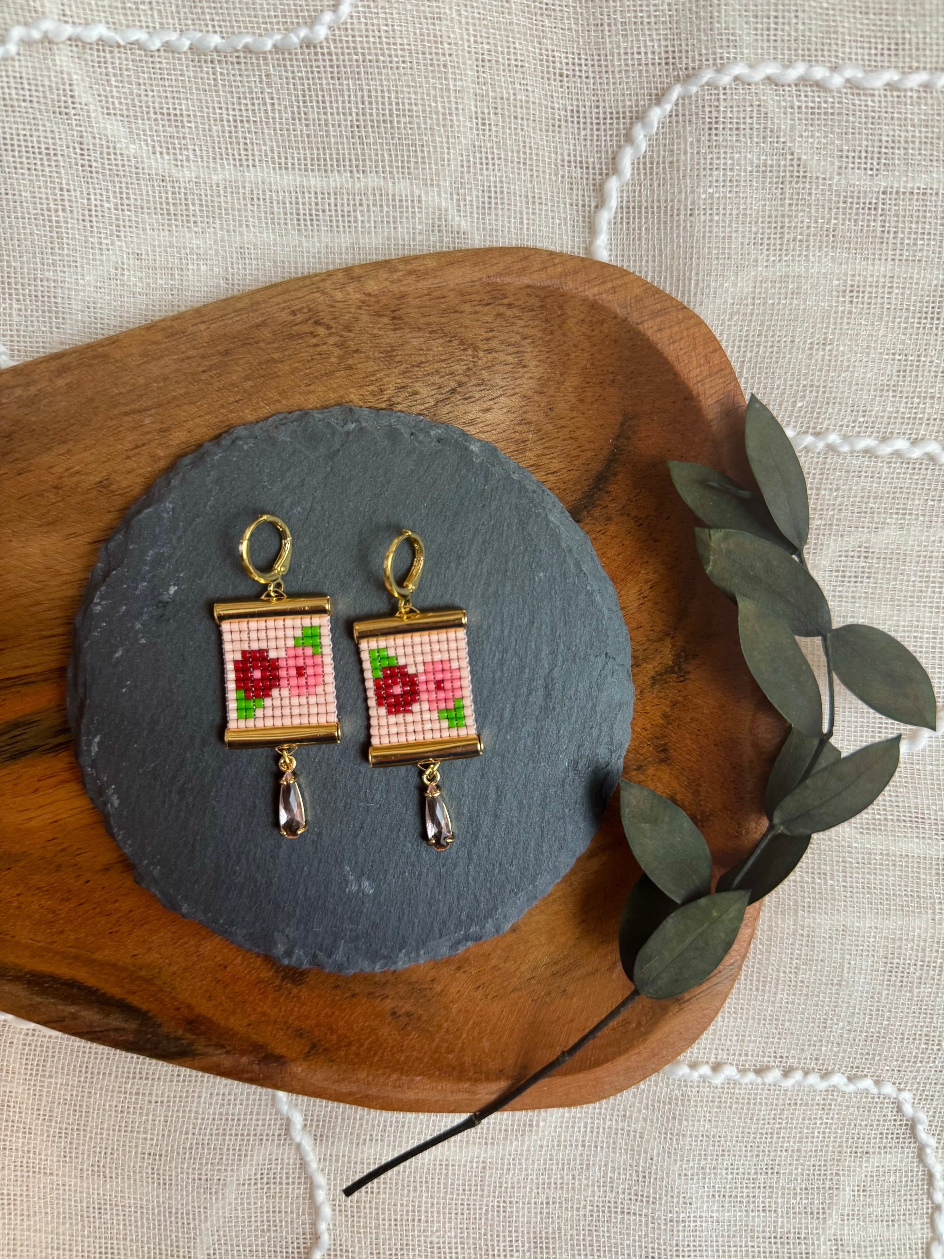 Pair of beaded earrings with floral design on a wooden and slate surface.