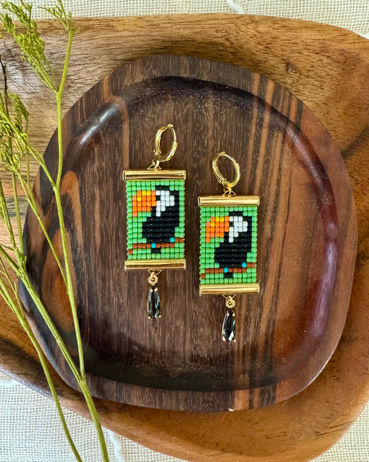 Toucan-themed beaded earrings on a wooden tray with a natural background