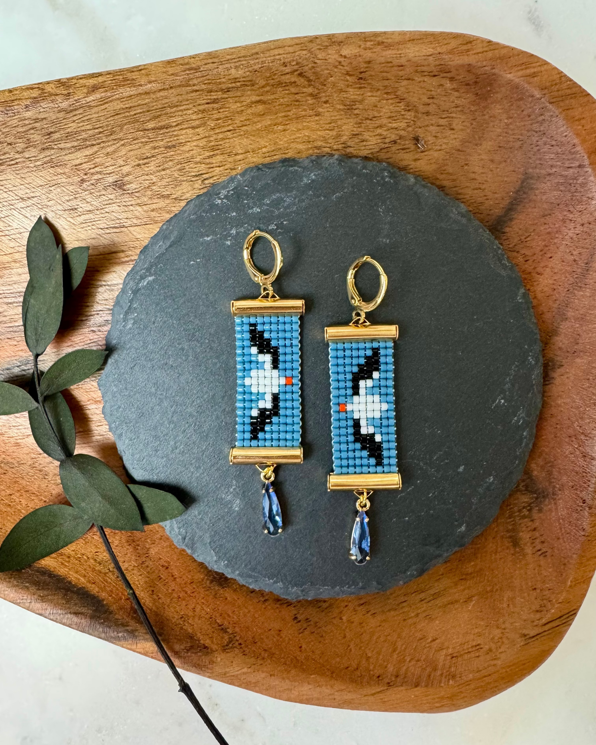 Abatross - themed beaded earrings on a slate stone with a wooden board and eucalyptus leaves.