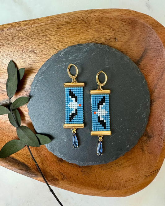 Abatross - themed beaded earrings on a slate stone with a wooden board and eucalyptus leaves.