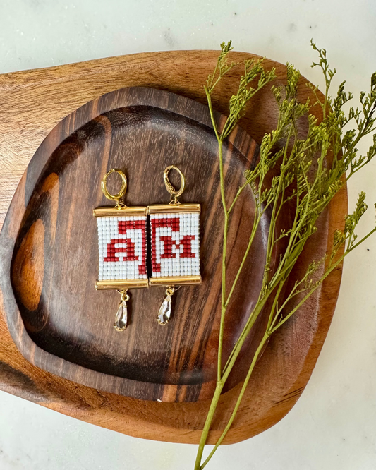 Earrings with 'A,T,M' design on a wooden tray with greenery