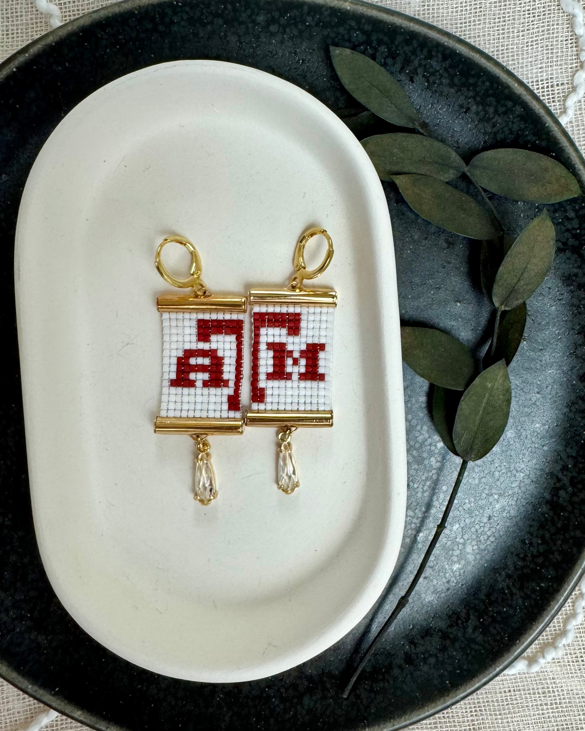 Earrings with 'A&M' design on a white dish with green leaves