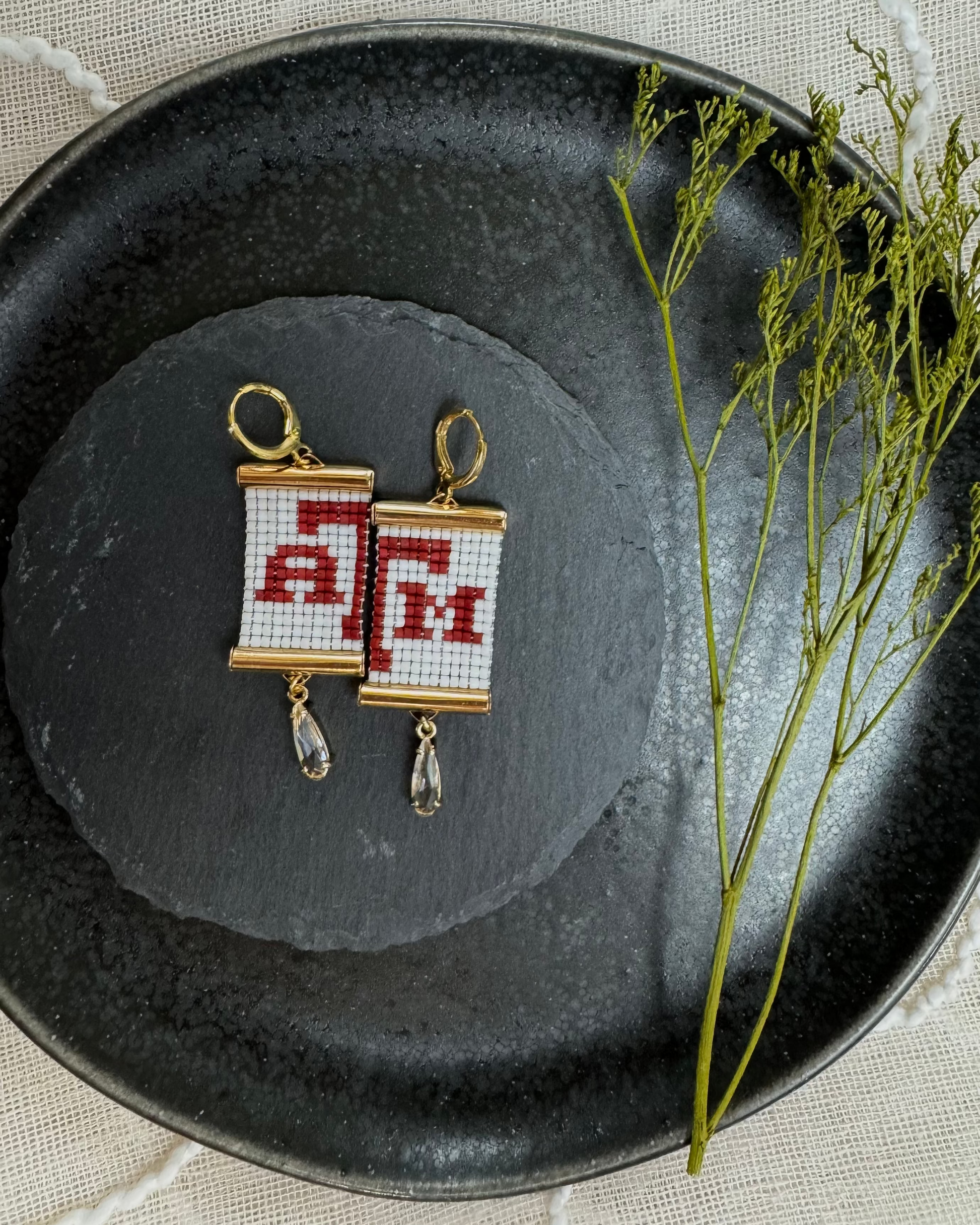 Earrings with 'A, T, M' design on a dark plate with a decorative background