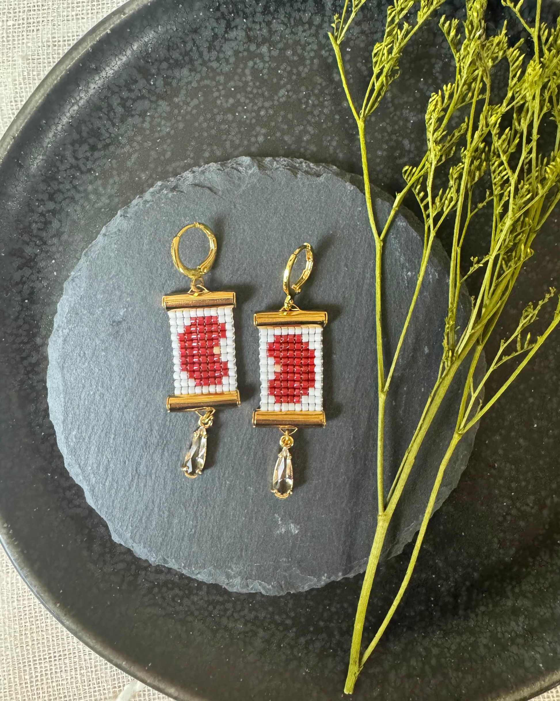 Pair of beaded earrings depicting kidney beans on a dark stone surface with a branch.