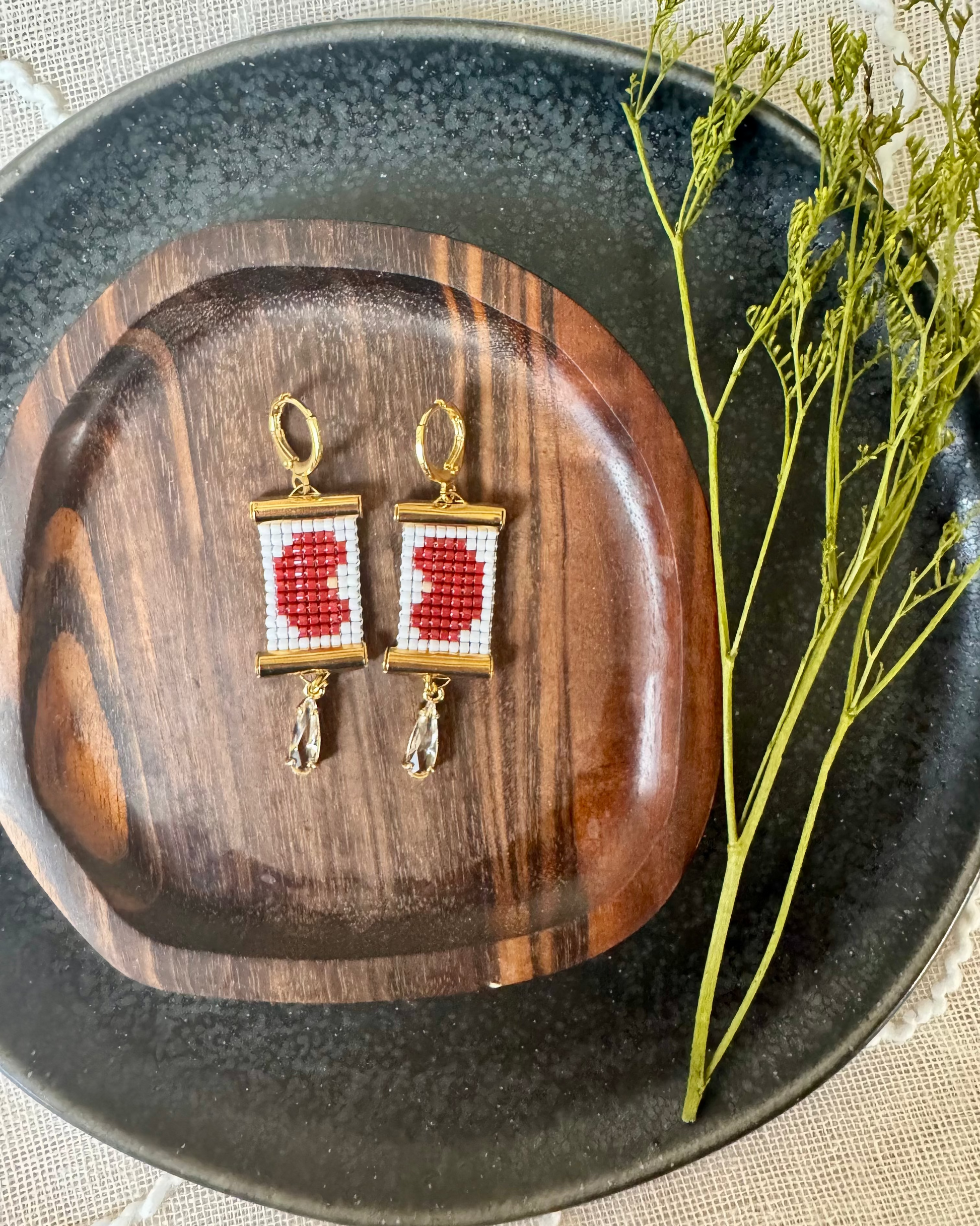 Pair of beaded earrings depicting kidney beans on a wooden plate with a decorative branch on a textured surface