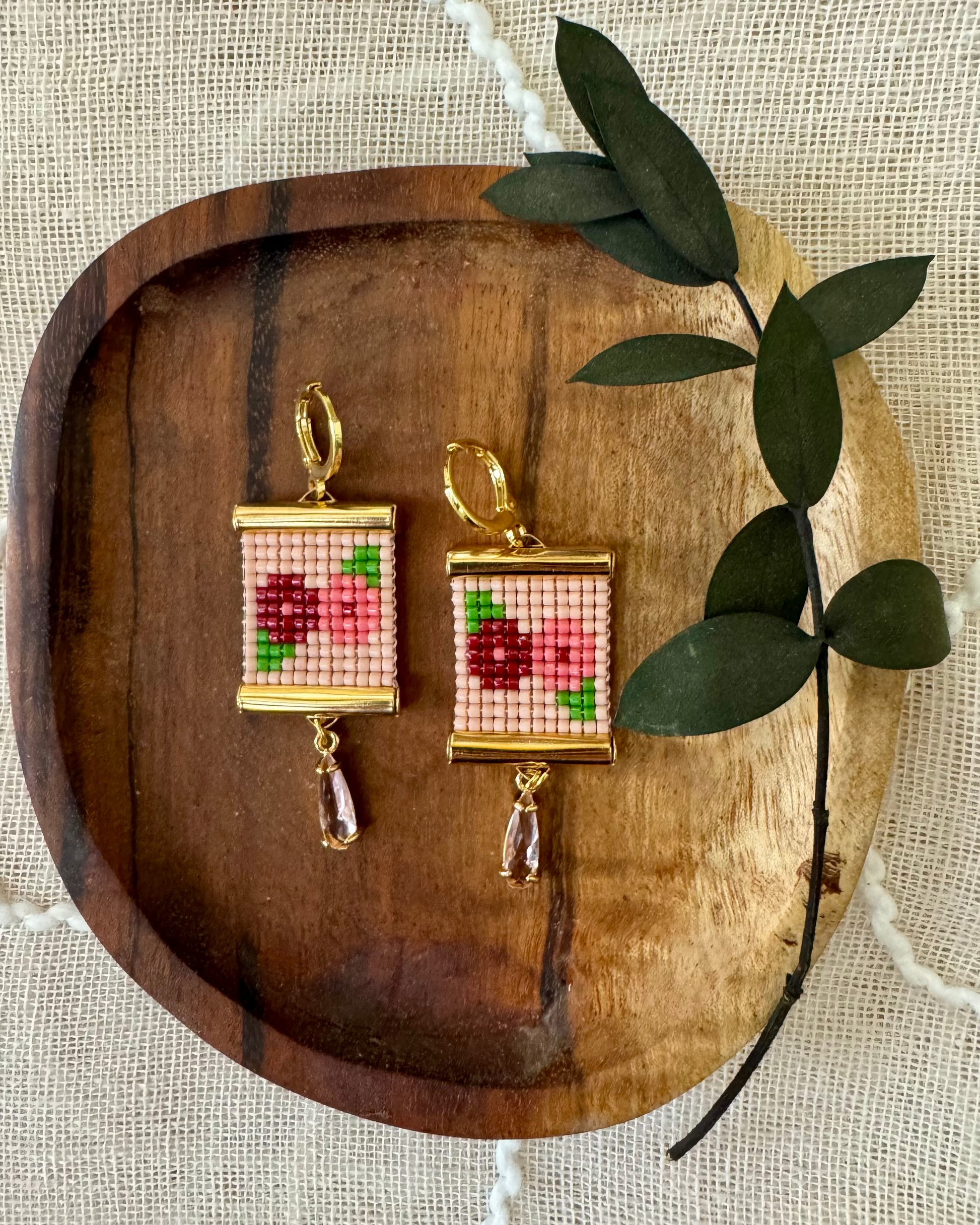 Beaded earrings depicting flowers on a wooden tray. 
