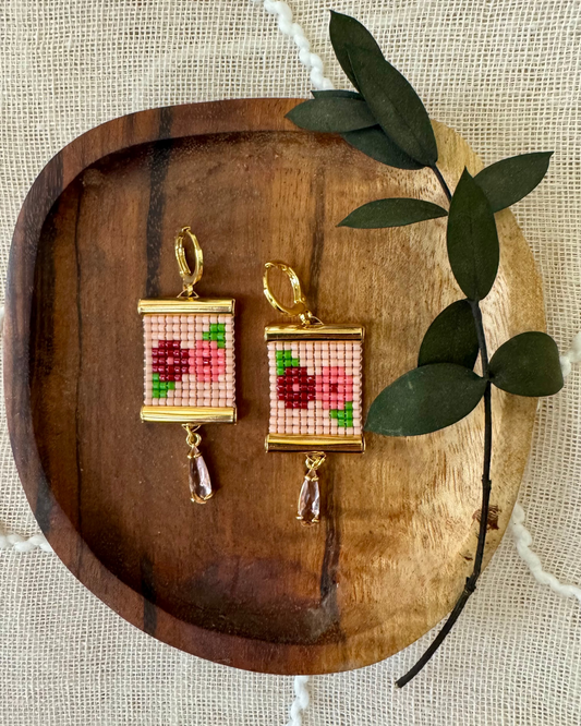 Beaded earrings depicting flowers on a wooden tray. 