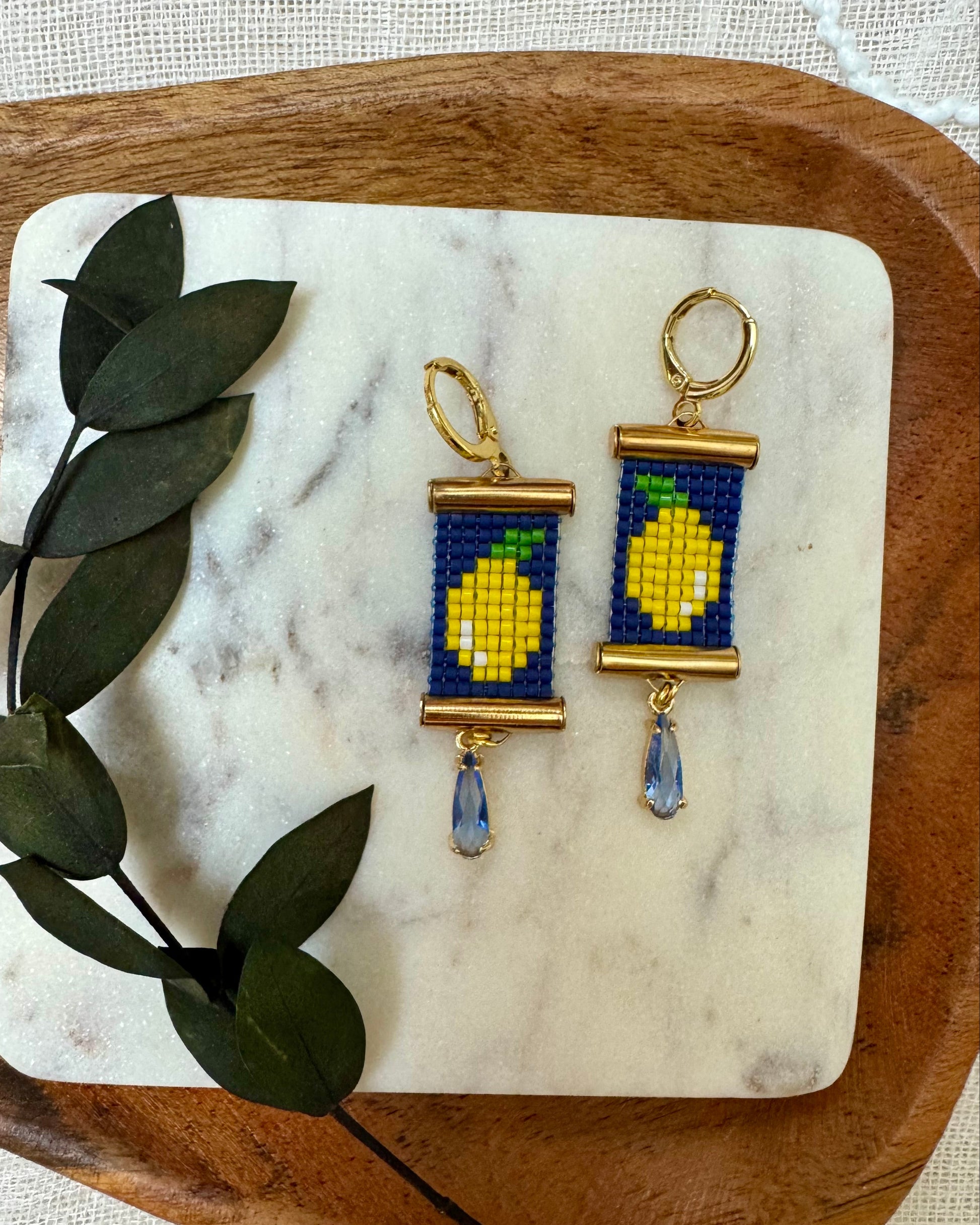 Pair of earrings with lemon design on a marble and wood surface