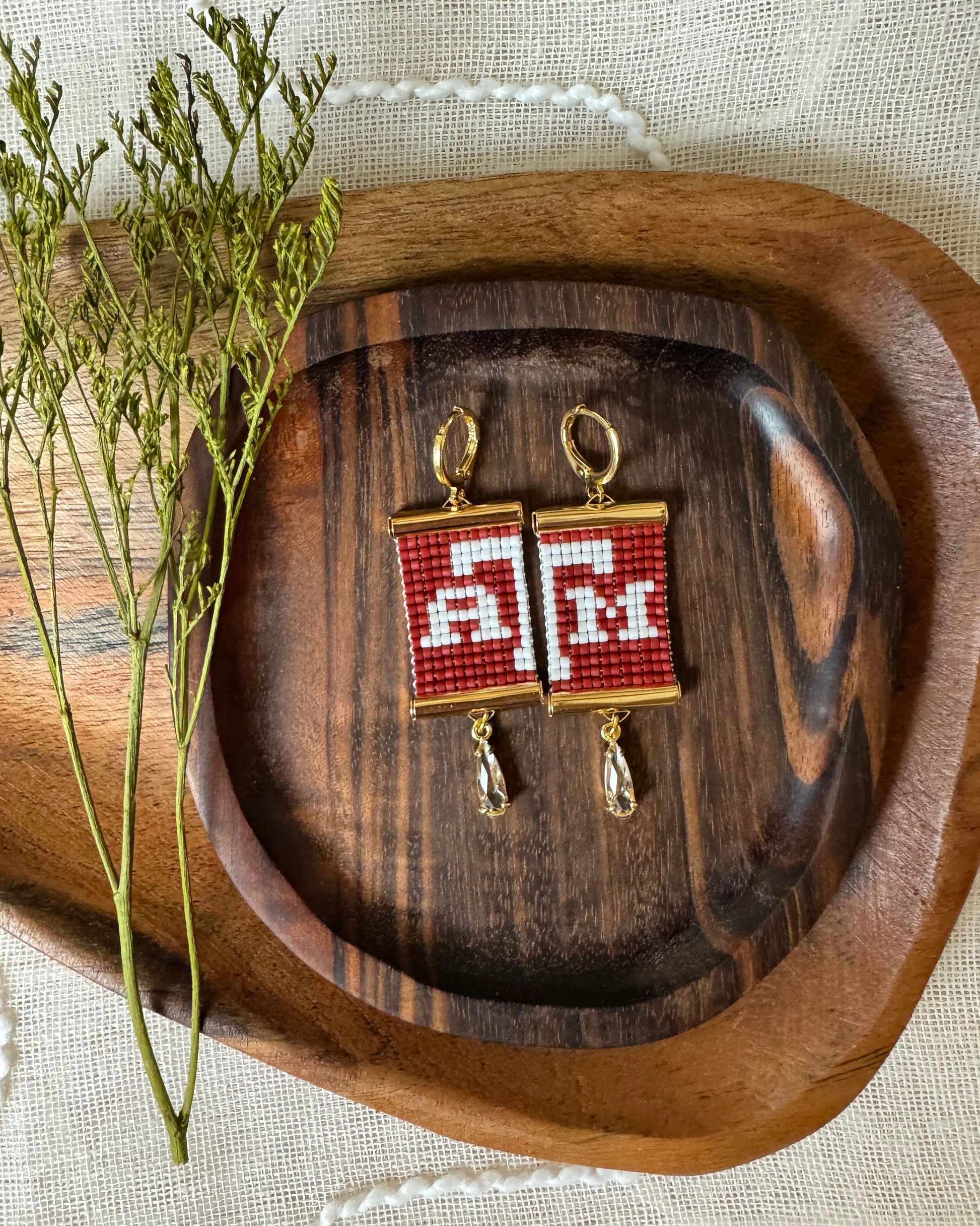 Pair of beaded earrings with red and white pattern on a wooden tray